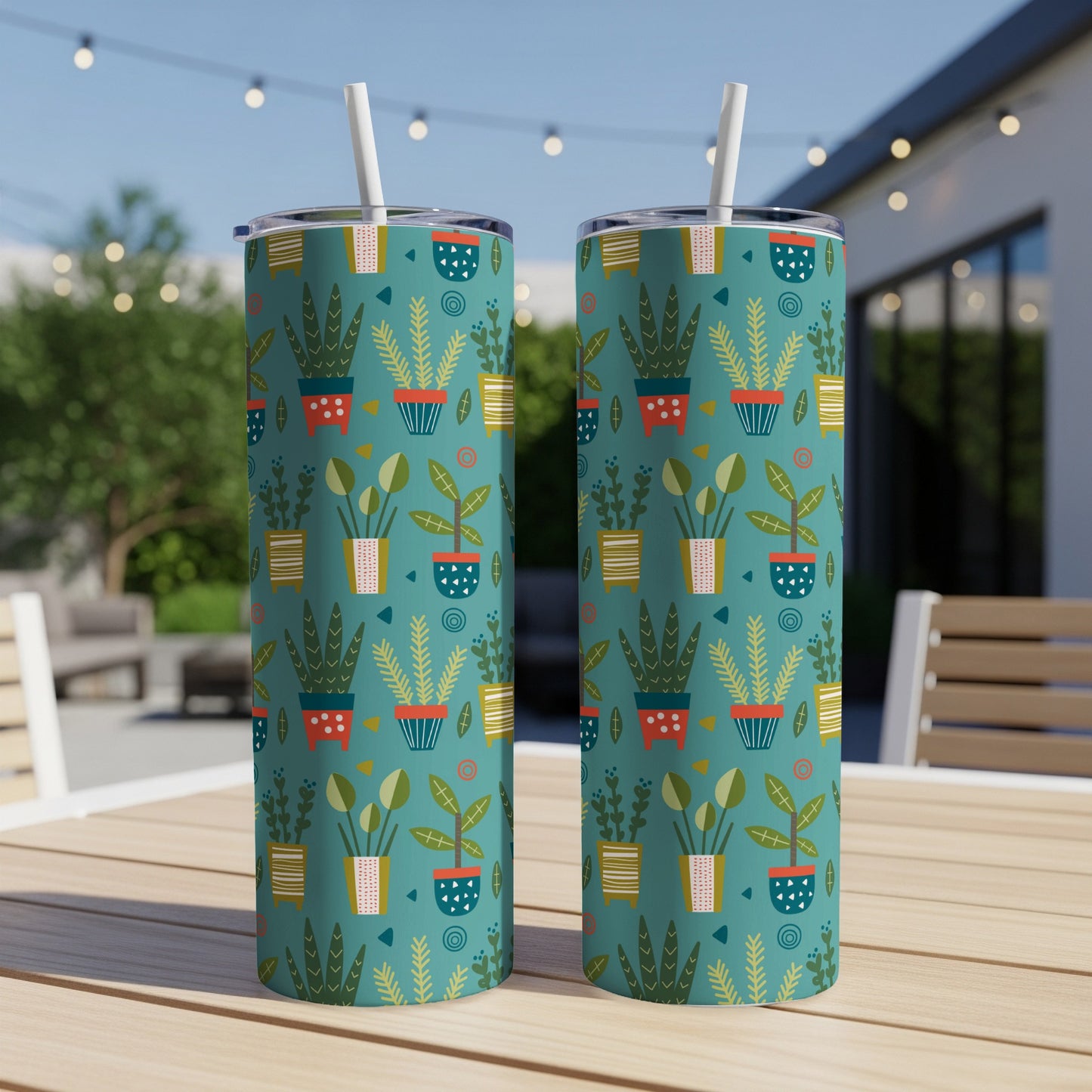 Two teal tumblers with a retro potted plant pattern and straws, resting on a wooden table.