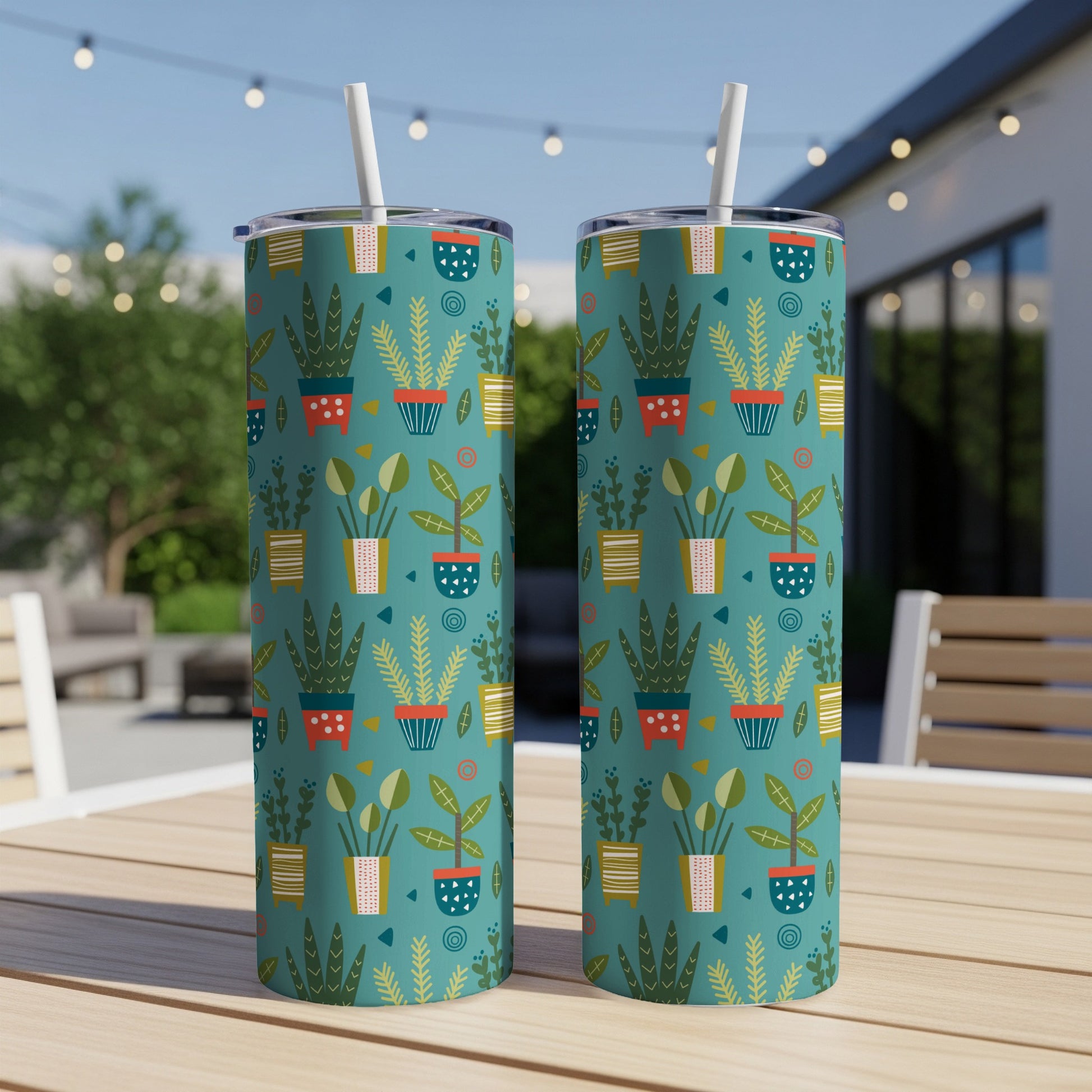 Two teal tumblers with a retro potted plant pattern and straws, resting on a wooden table.