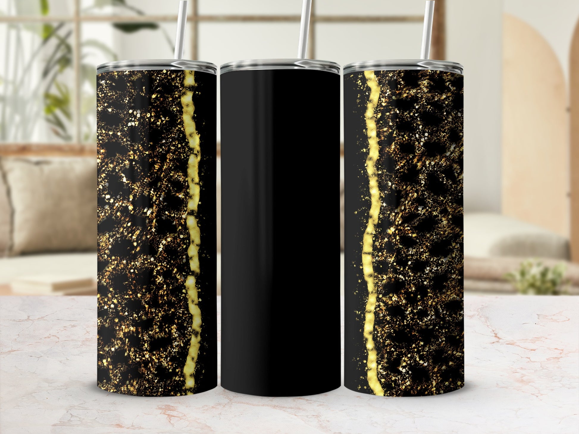 Black tumbler with gold glitter accent and straw, shown on a marble surface.