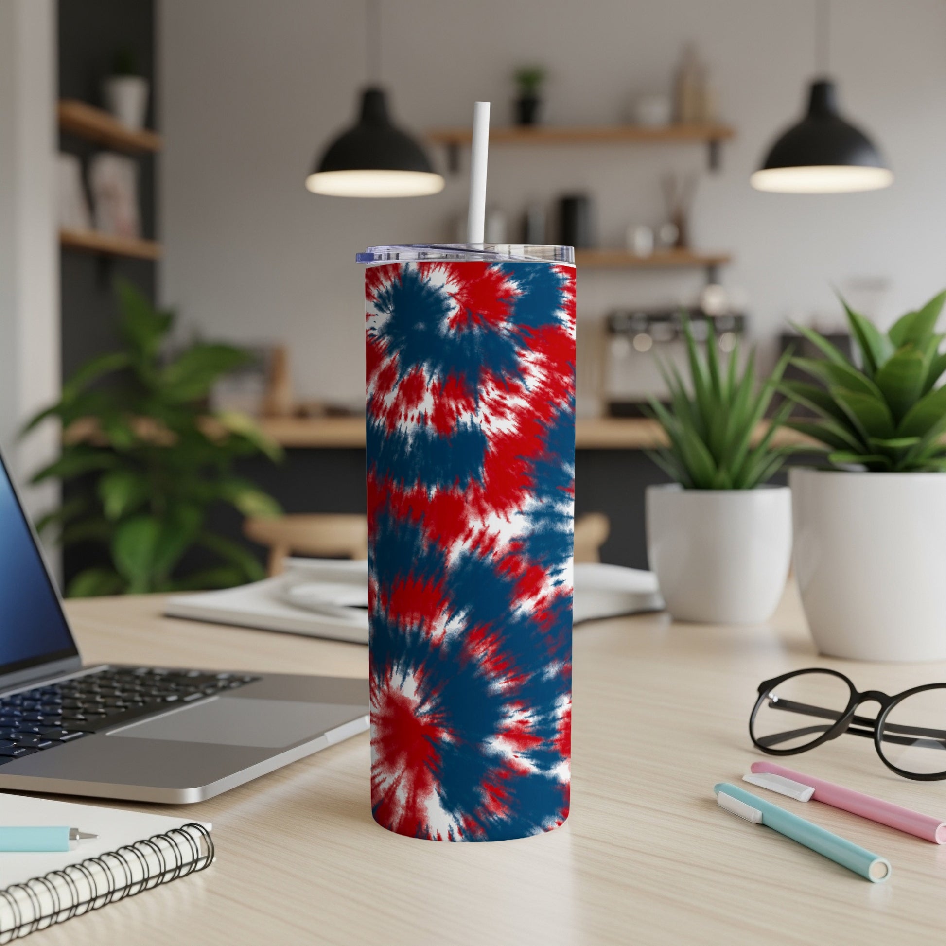 Tumbler with red, white, and blue tie-dye pattern and white straw on a wooden desk.