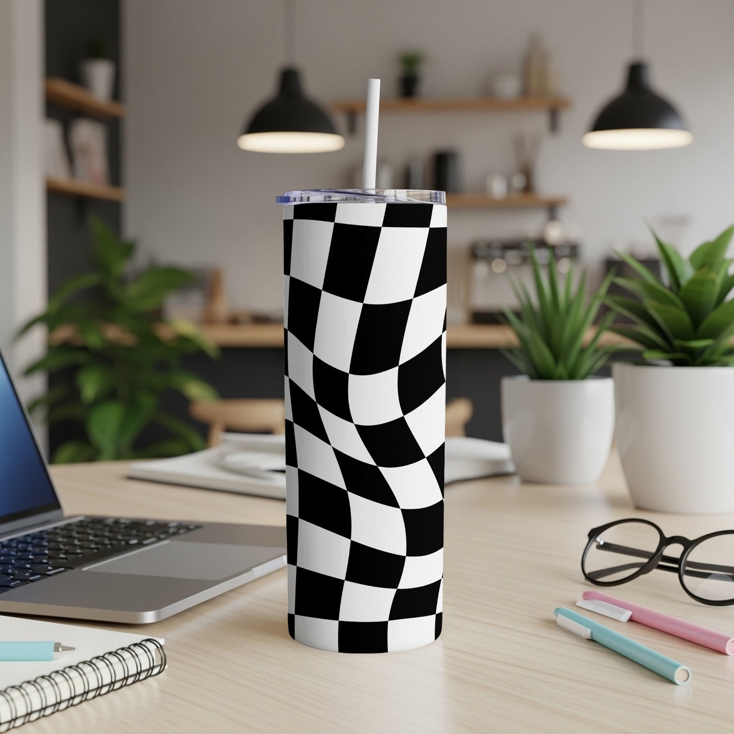 Black and white checkered tumbler with a straw on a desk.