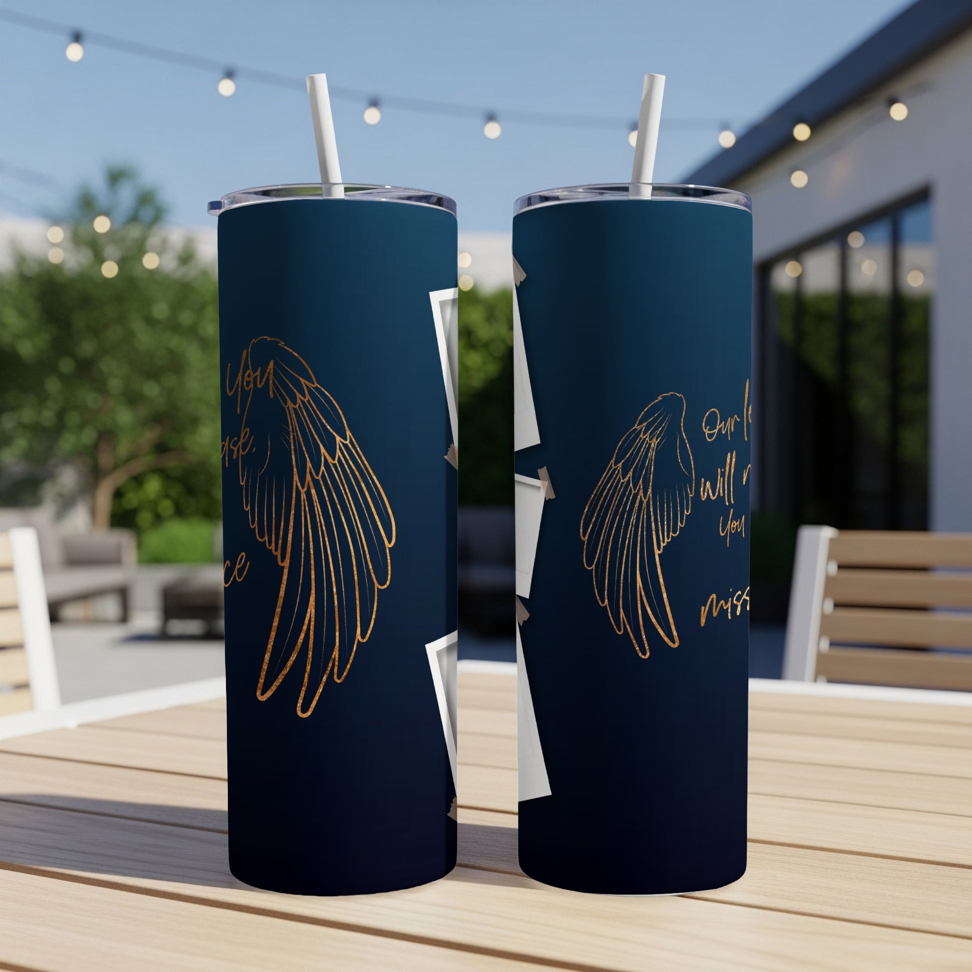 Two dark blue tumblers with gold wings and text on outdoor table.