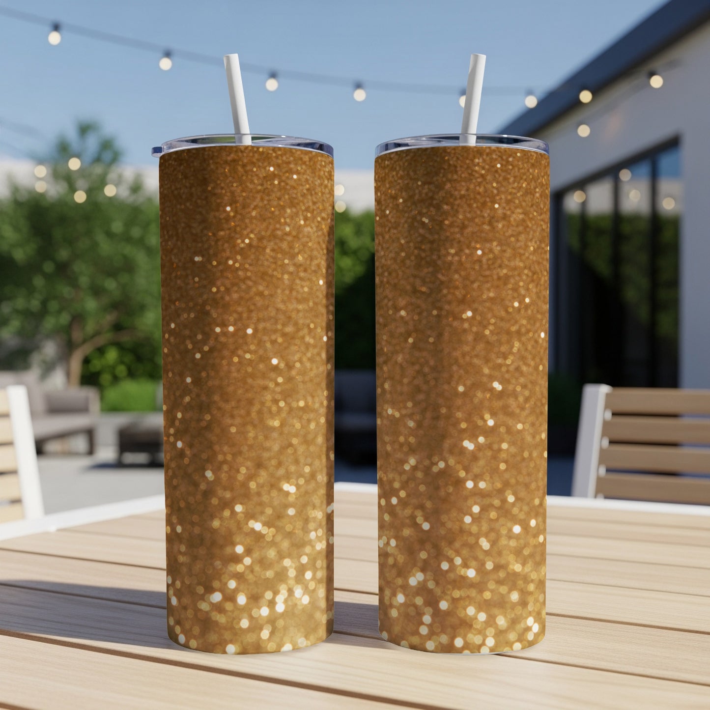 Two tall, gold glitter tumblers with straws on a wooden table.