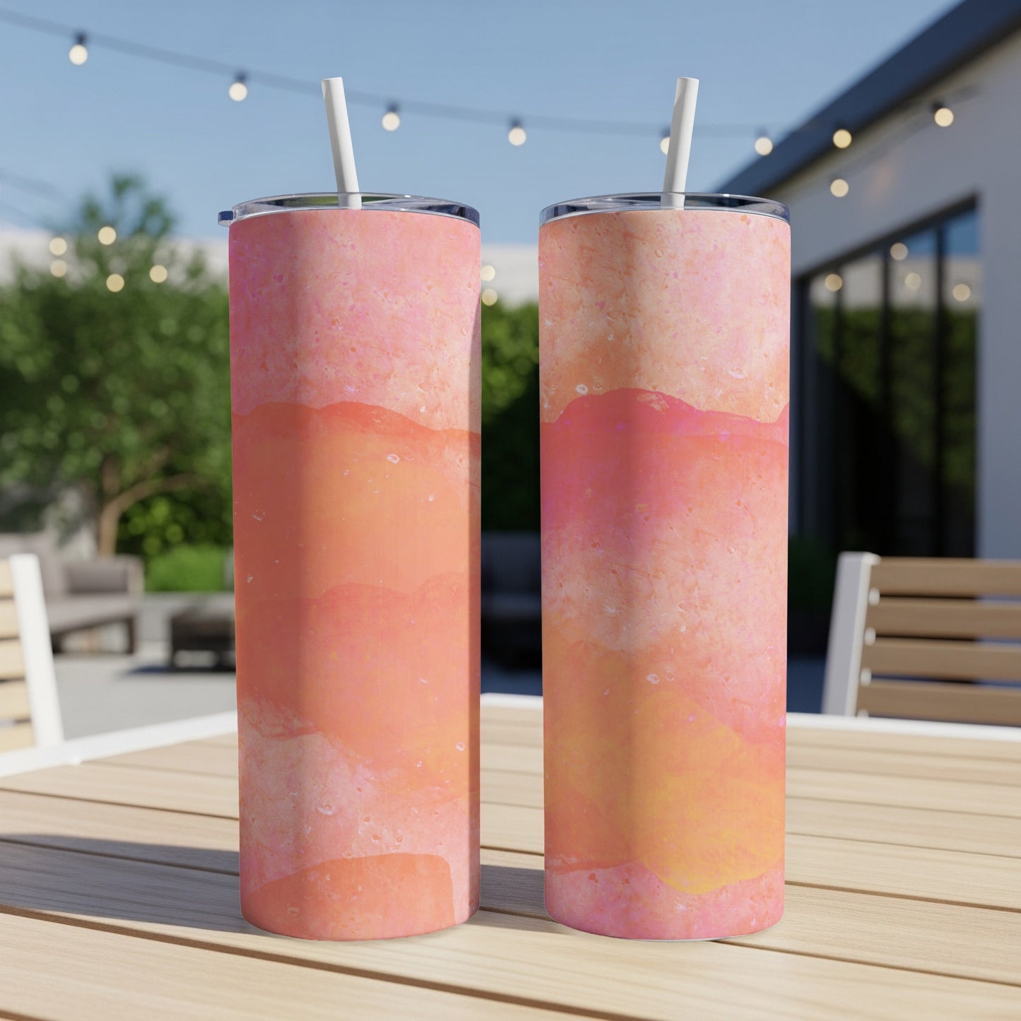Two tall, skinny tumblers with a pink and orange watercolor design sit on a table.