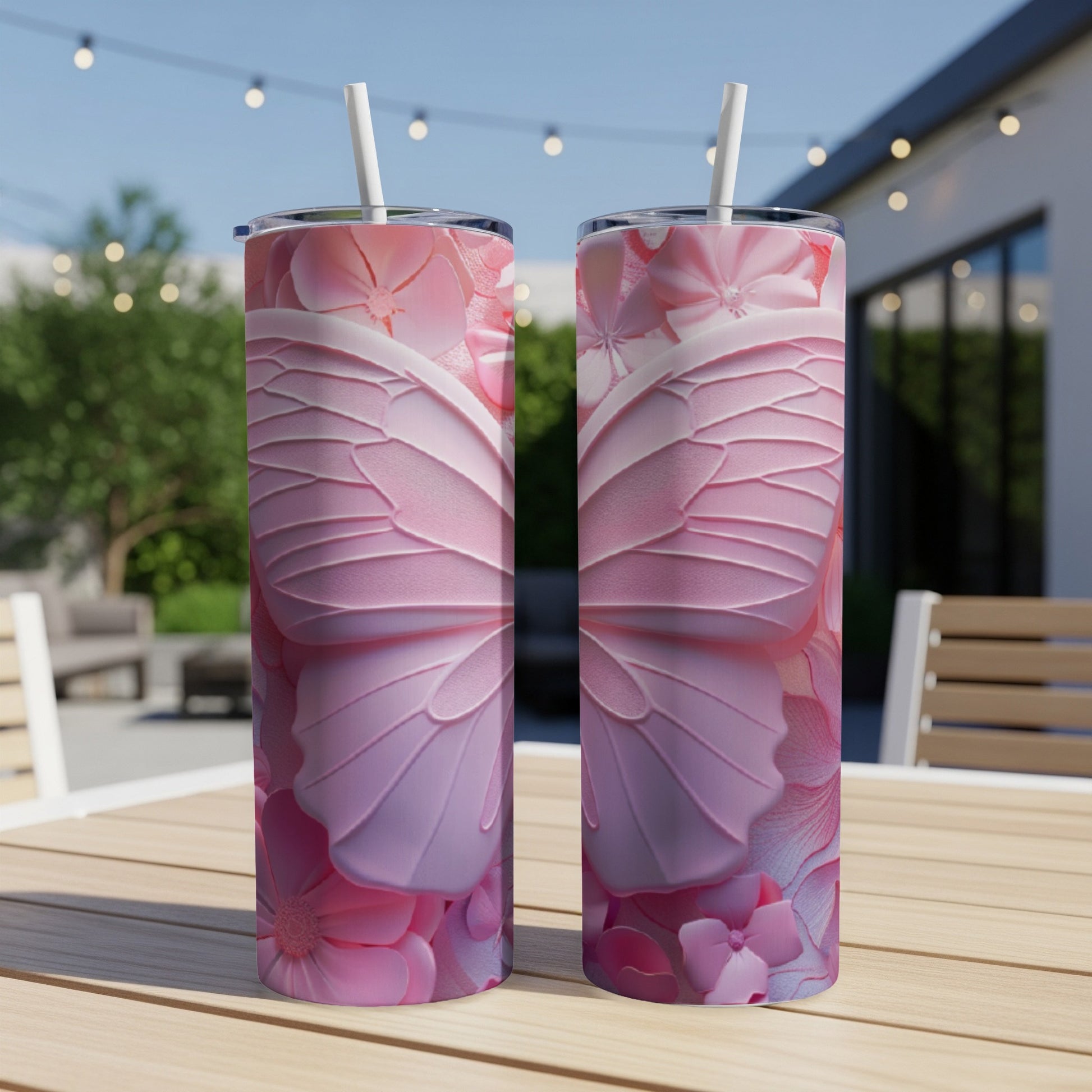 Two pink butterfly wing patterned tumblers with straws on a wooden table.