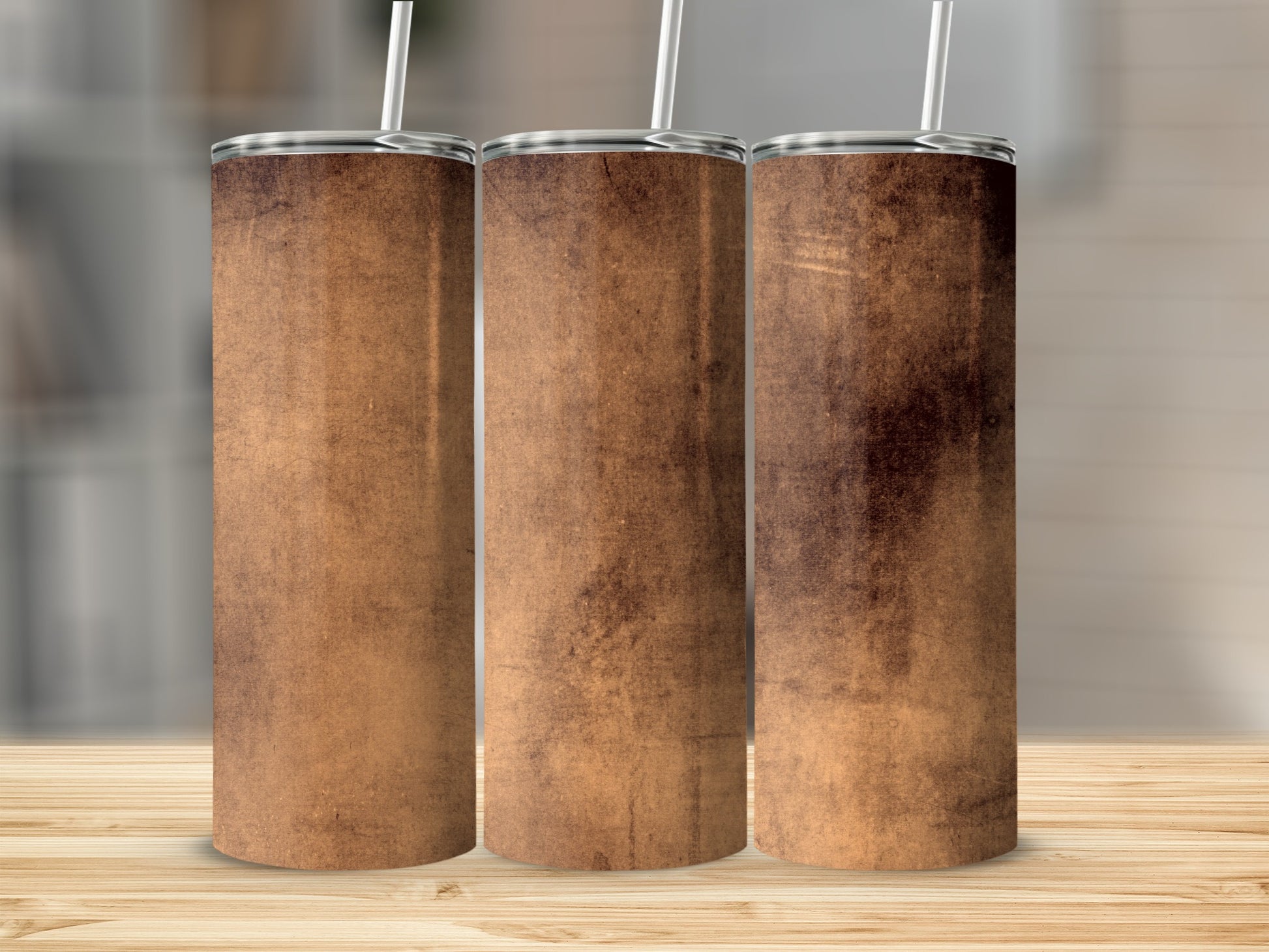 Three tumblers with a distressed brown texture and straws stand on a wooden surface.