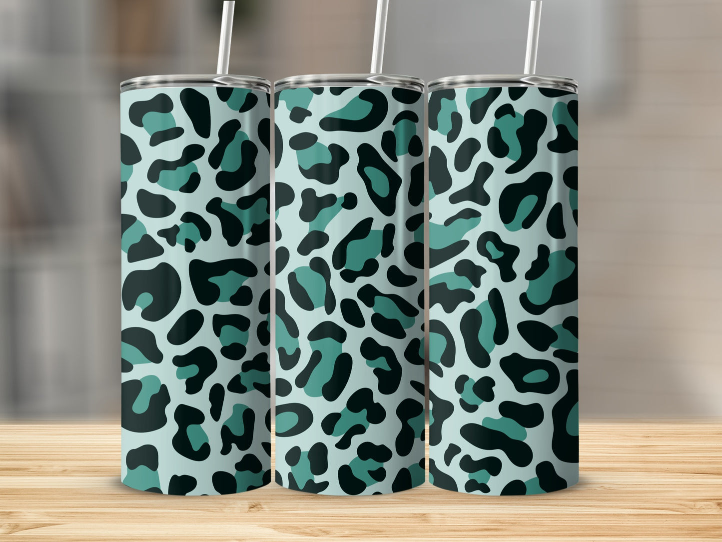 Three tumblers with teal and black leopard print designs stand on a wooden surface.