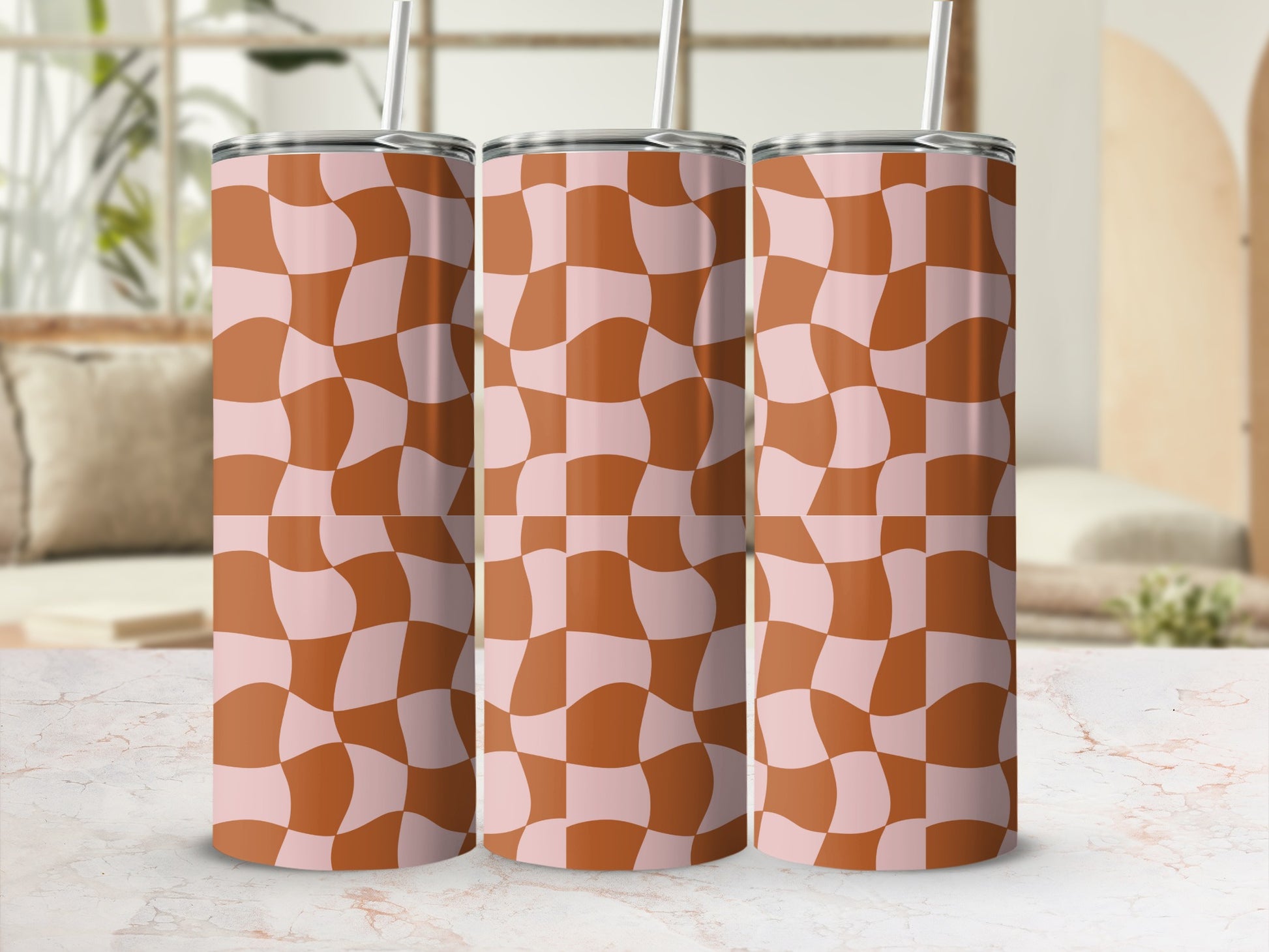 Three pink and tan checkered tumblers with straws stand in front of a blurred background.