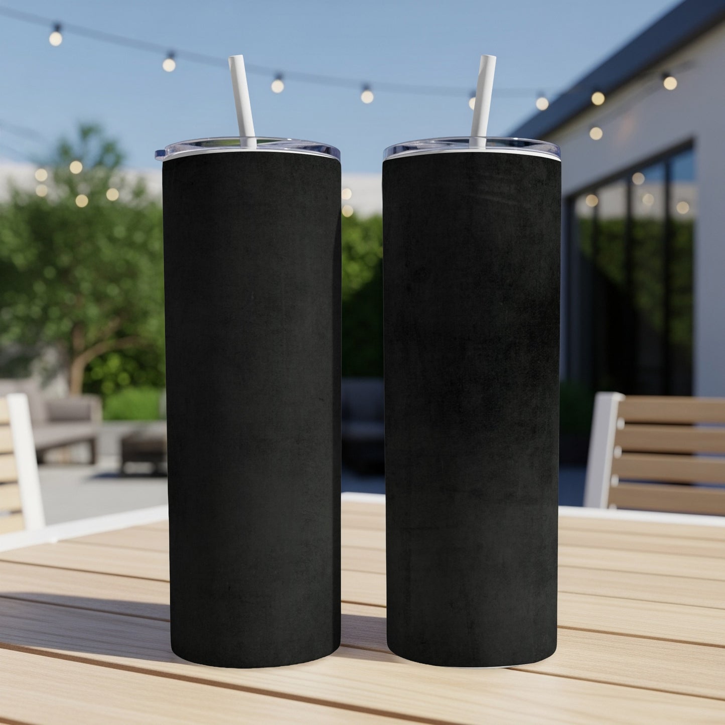 Two black tumblers with white straws on a wooden table outdoors.