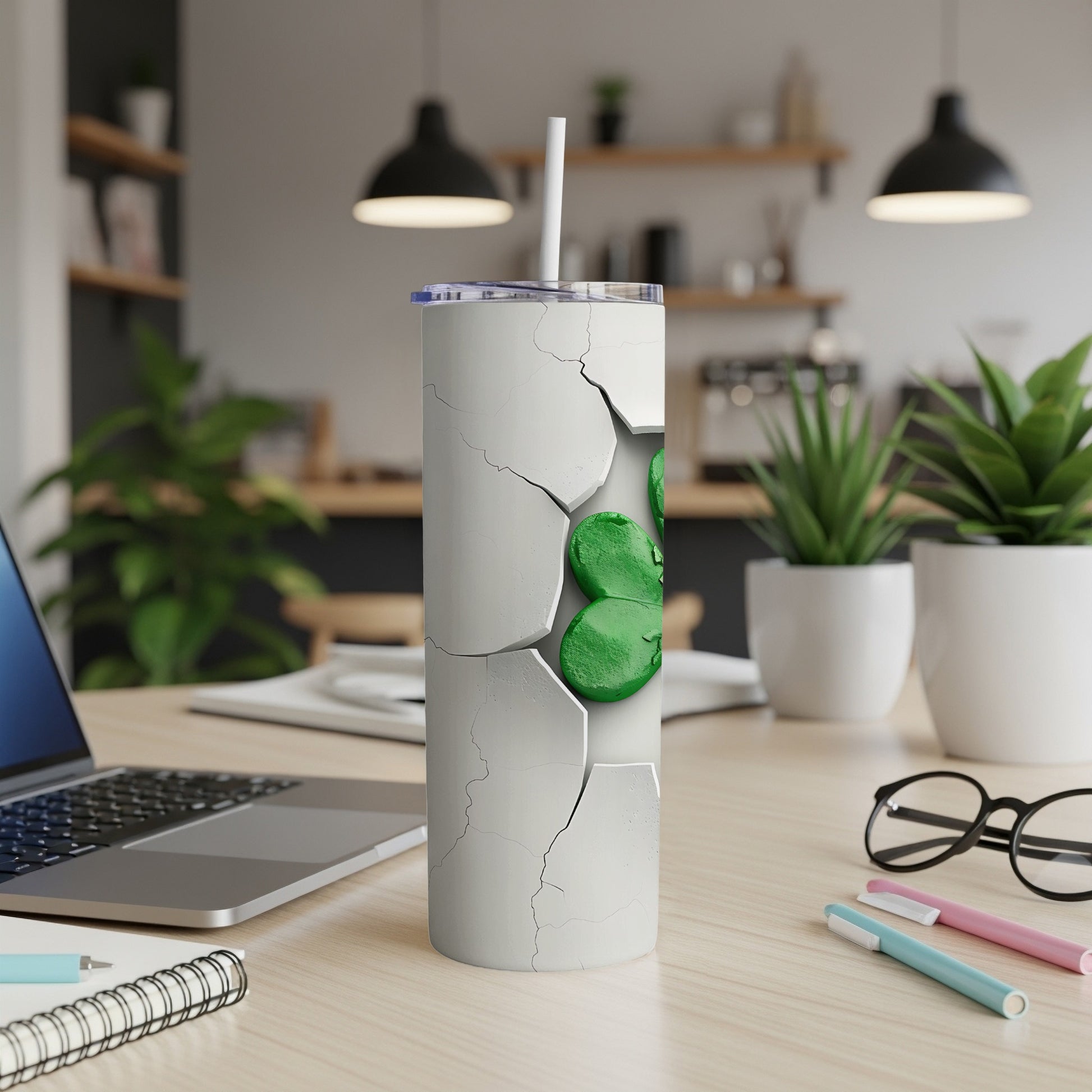 White tumbler with green shamrock pattern and straw on a desk.