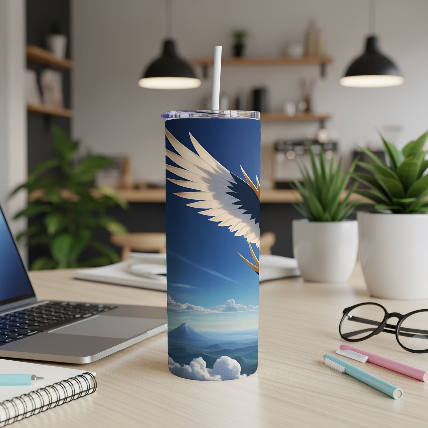 Blue tumbler with feathered wings against a sky with mountains.