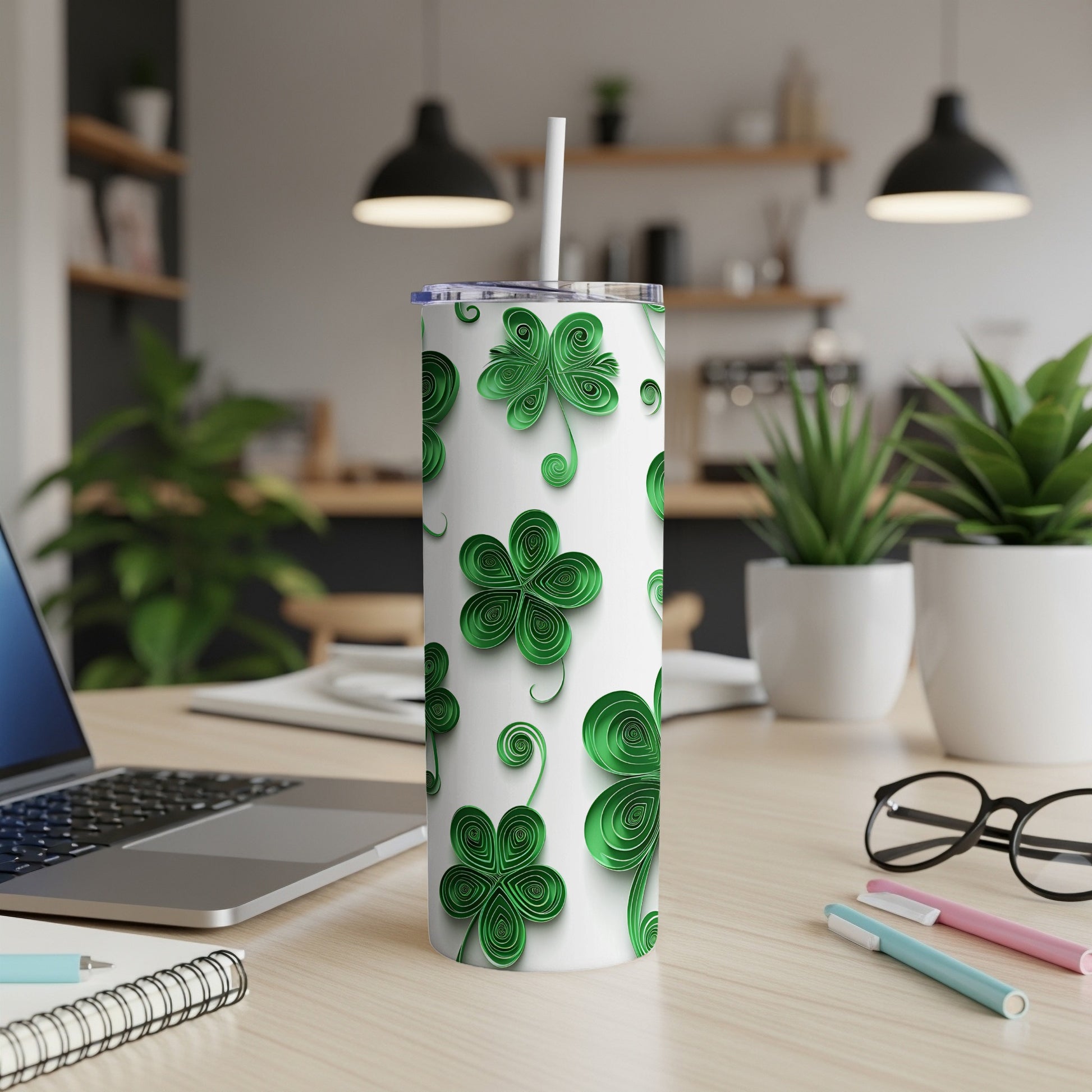 White tumbler with green shamrock pattern and straw, on a desk.