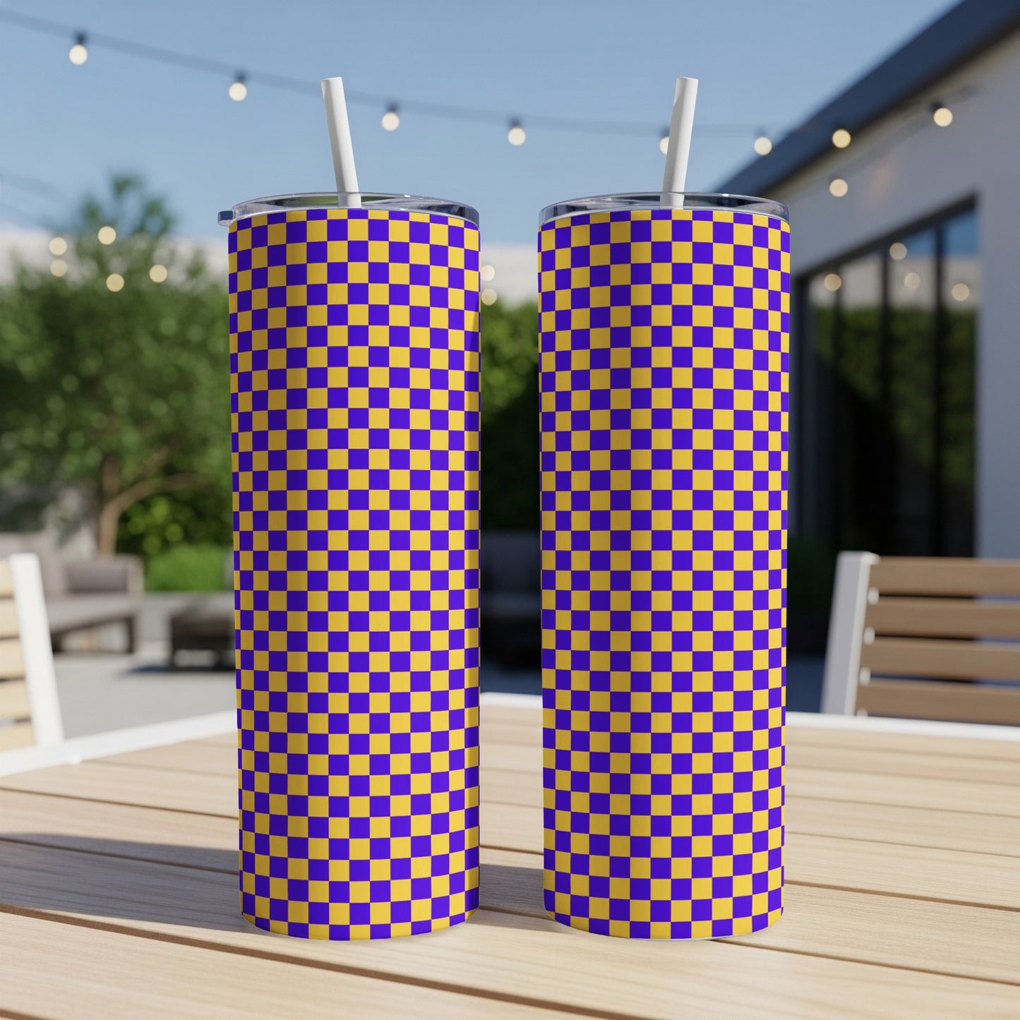 Two purple and gold checkered tumblers with straws on a wooden table.