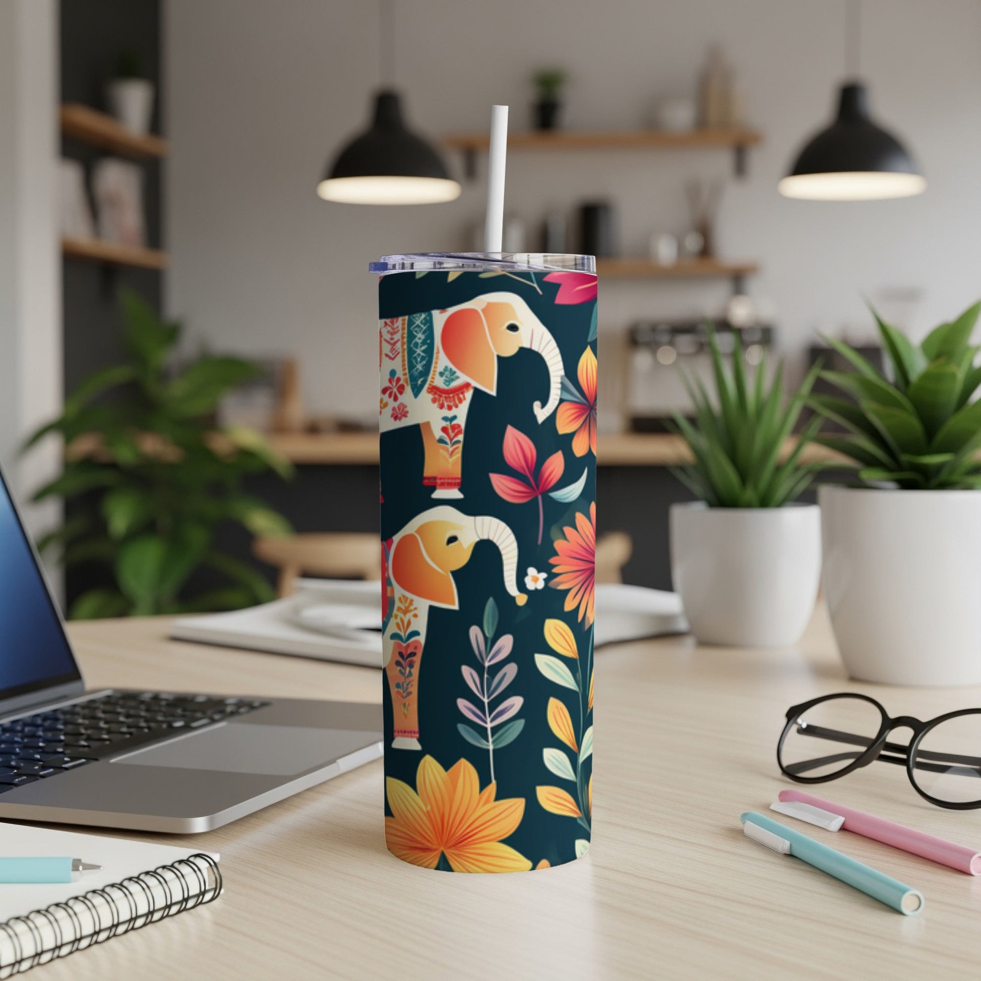 Tall tumbler with elephants and floral pattern, on a desk.