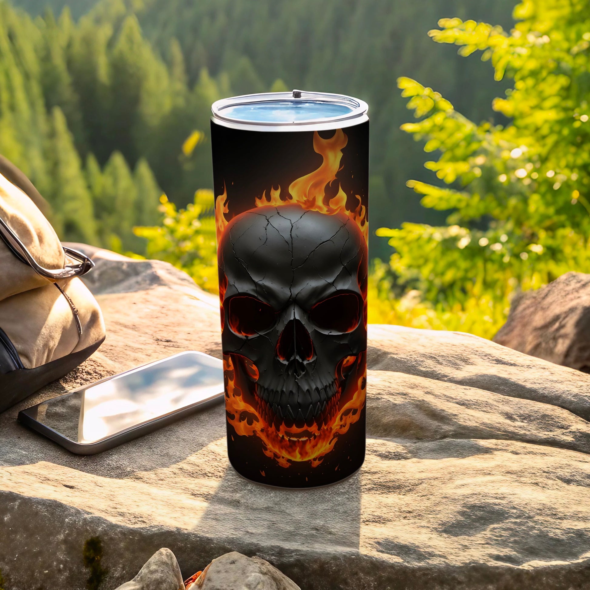 Black skull with flames on a tumbler next to a backpack and phone.