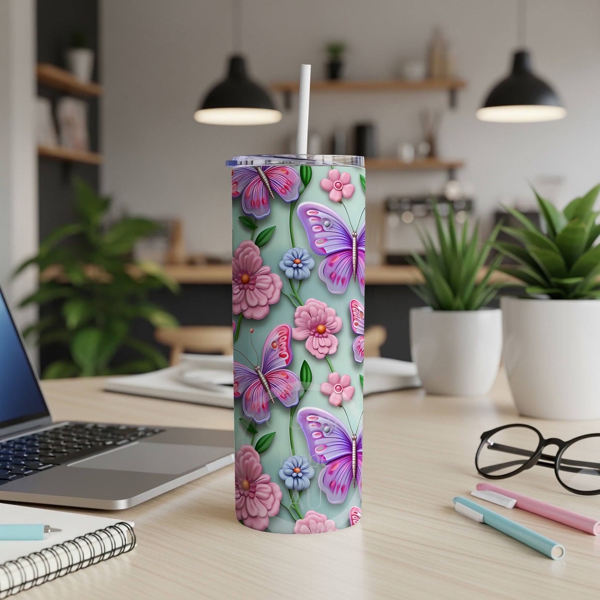 Mint green tumbler with butterflies and flowers, on a desk with laptop.
