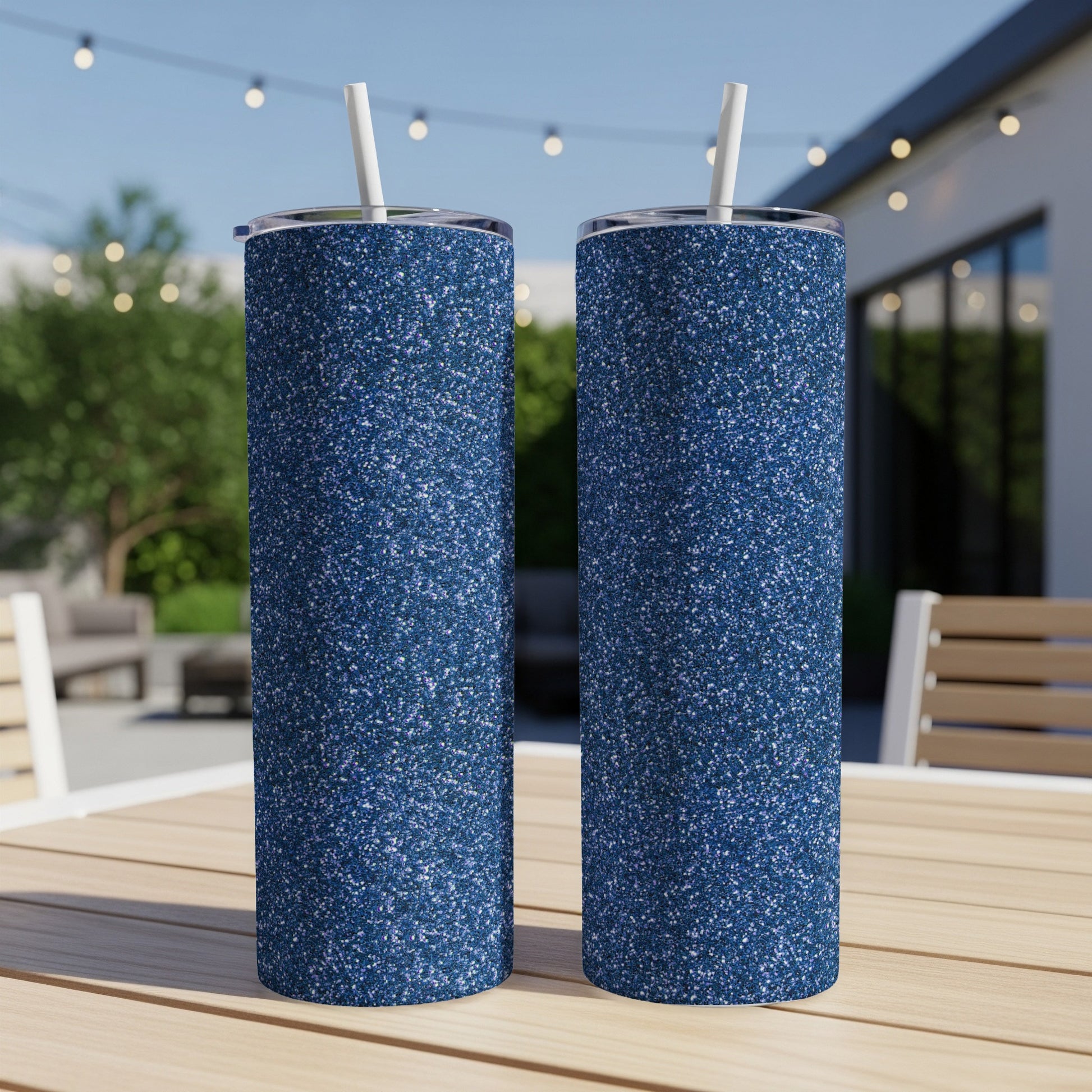 Two navy blue glitter tumblers with white straws sit on a wooden table.