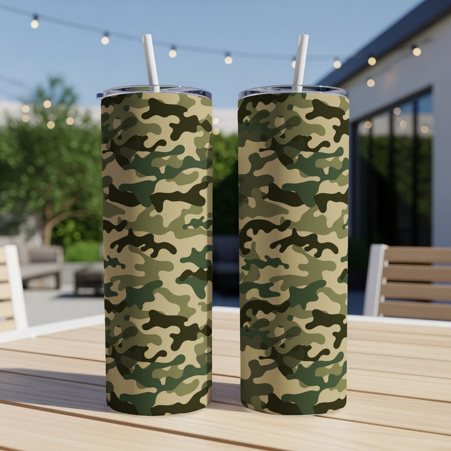 Two camouflage pattern tumblers with white straws on a wooden table outdoors.
