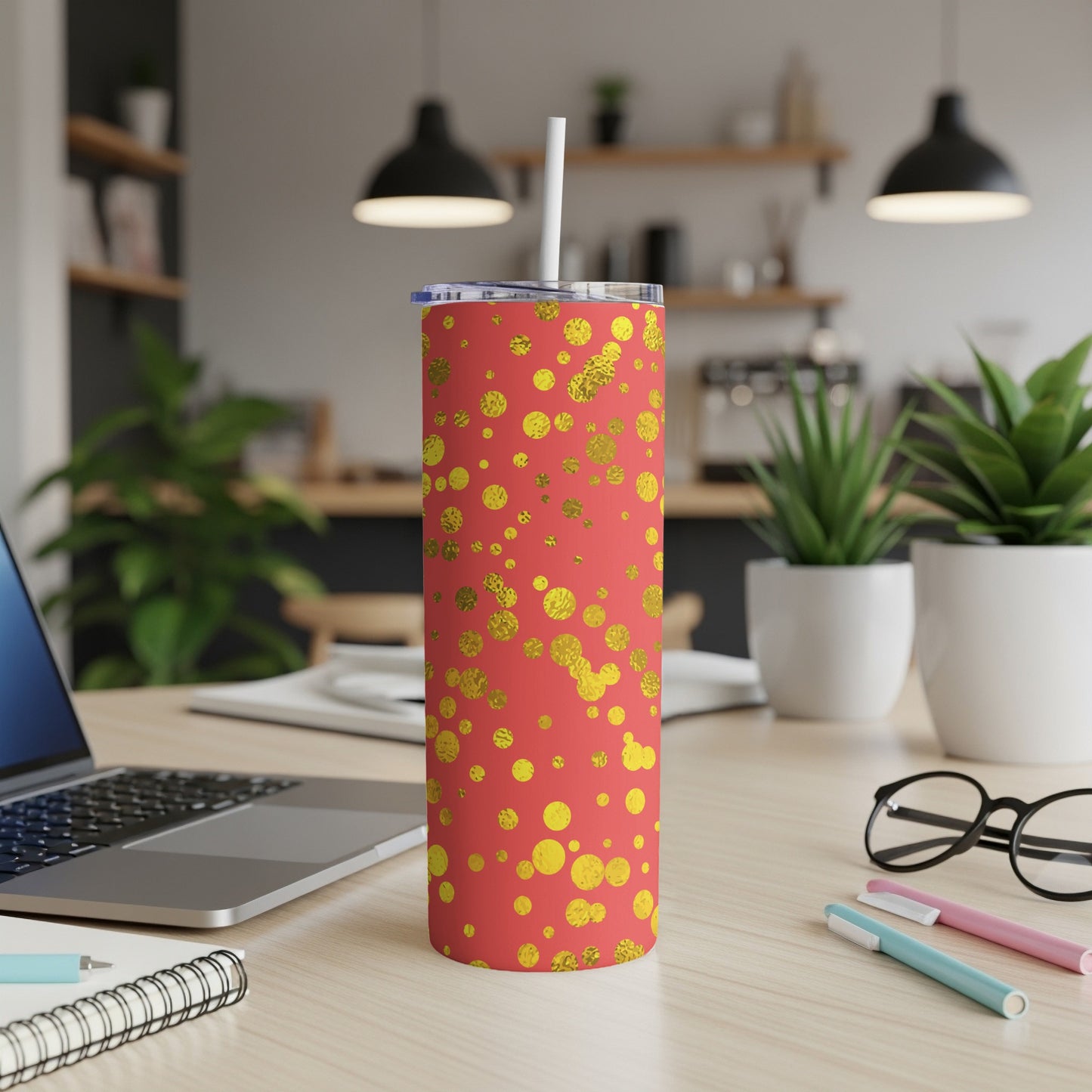 Coral tumbler with gold polka dots, white straw, on a desk.