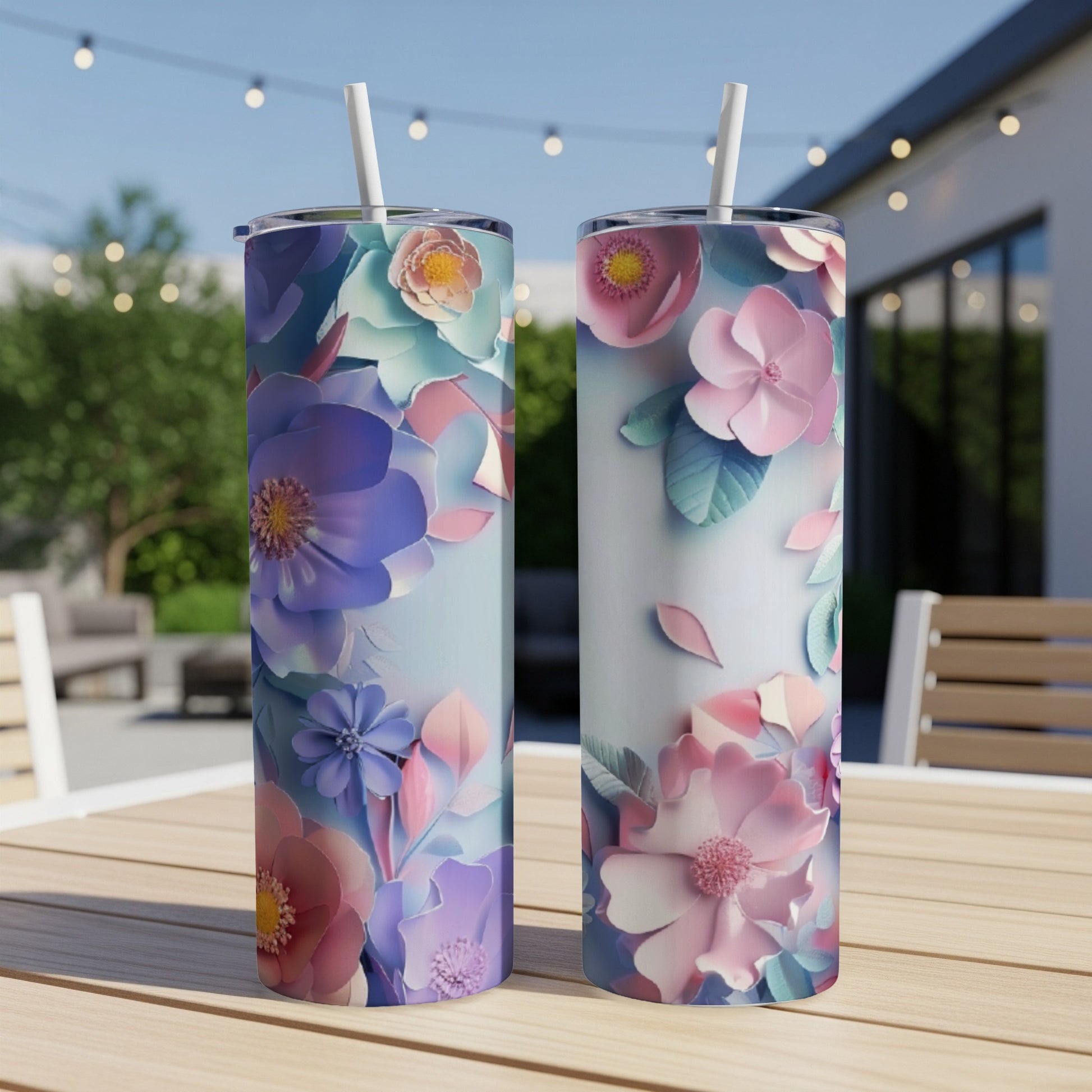 Two tall tumblers with colorful floral designs sit on a wooden table outdoors.