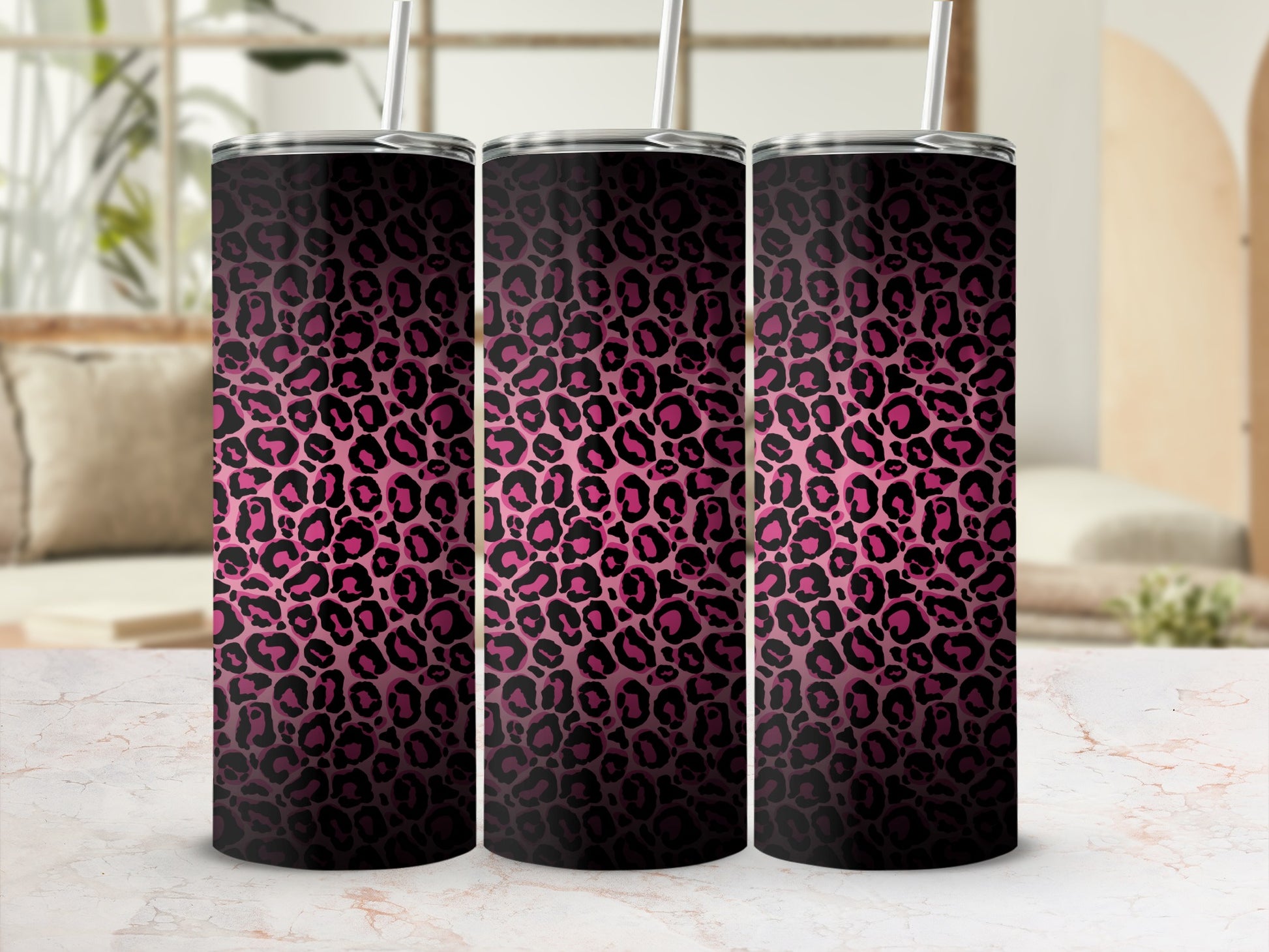 Three pink leopard print tumblers with straws on a marble surface.