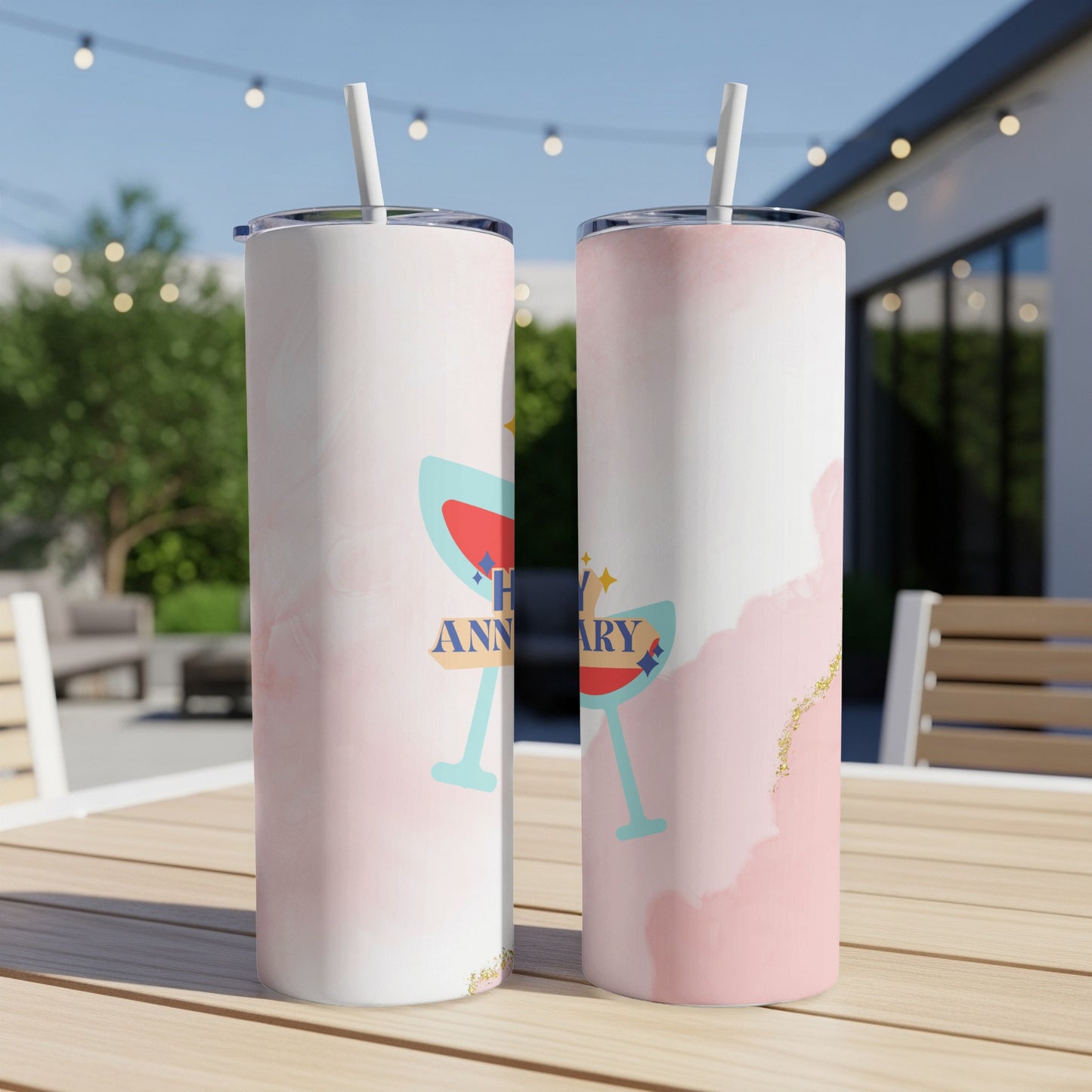 Two tumblers with "Happy Anniversary" and champagne glasses, set outdoors.