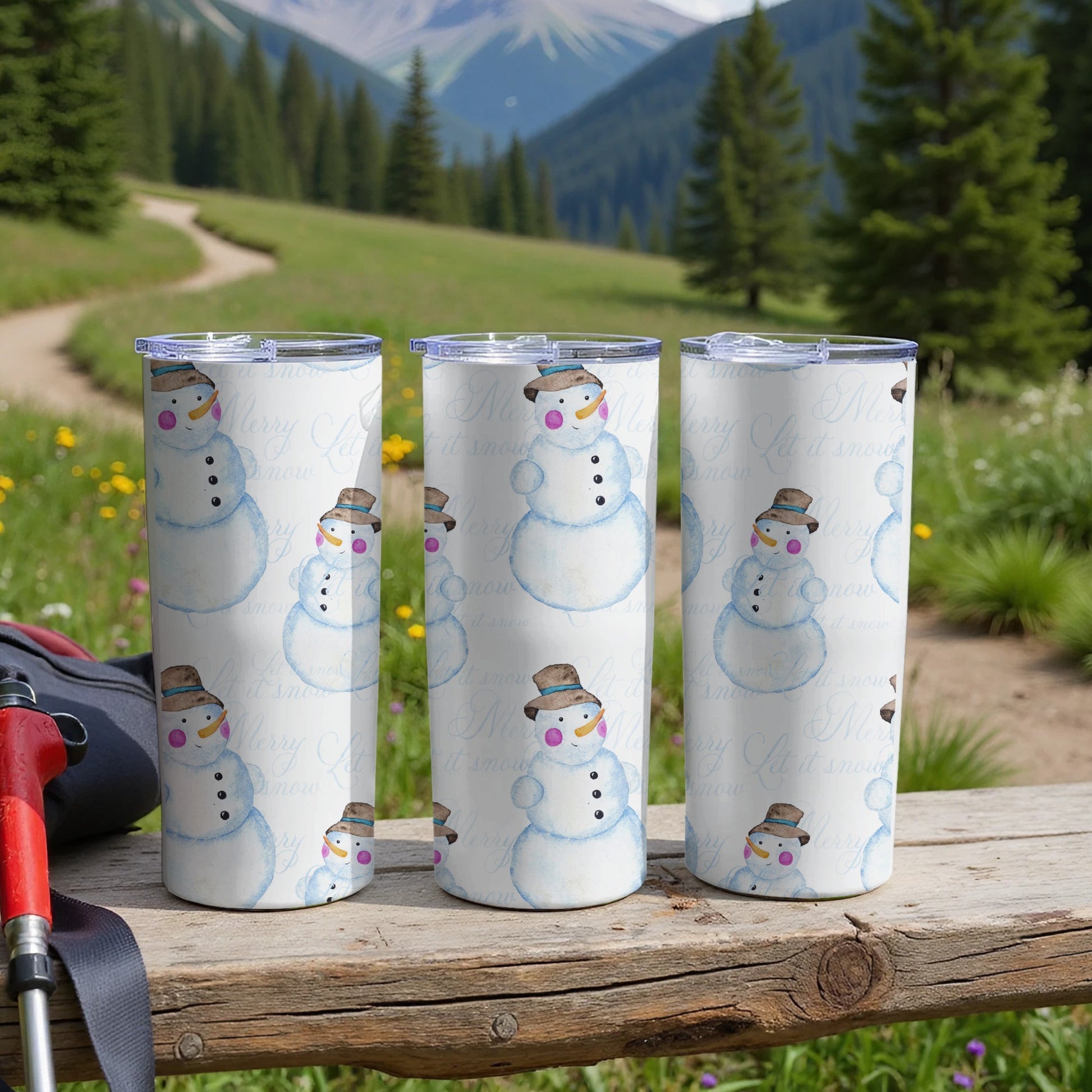 Three snowmen tumblers with "it snow" text on a wooden table.