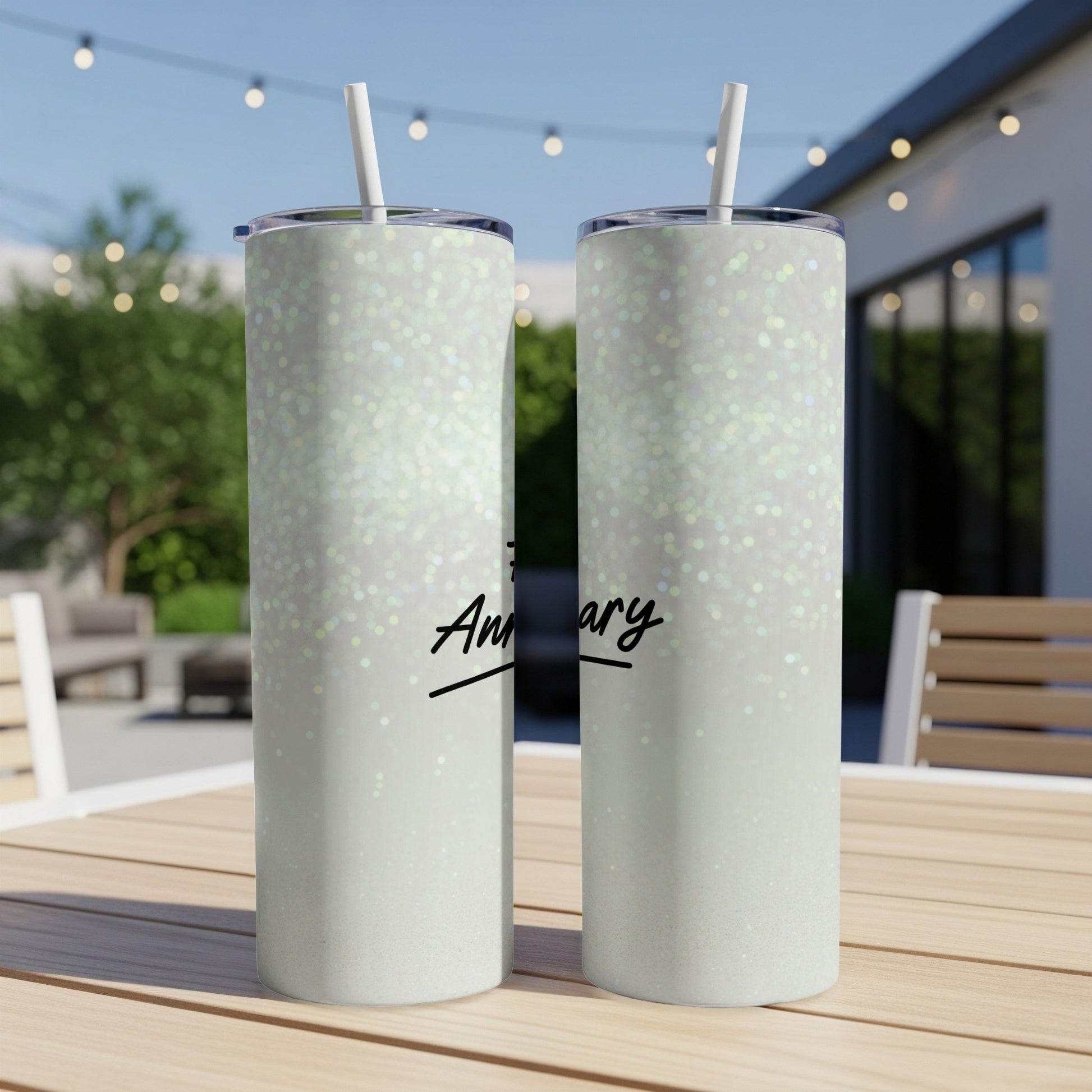 Two glittery tumblers with "Anniversary" text sit on an outdoor table.
