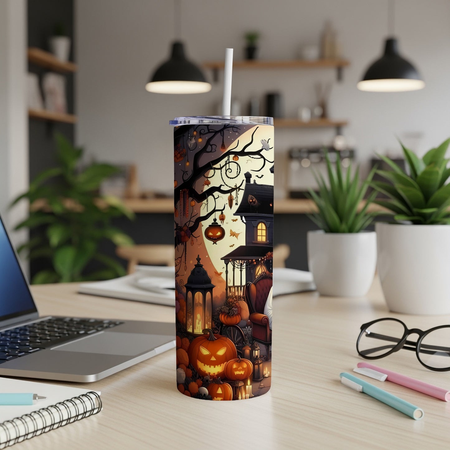 Halloween tumbler with pumpkins, ghosts, and haunted house scene on a desk.
