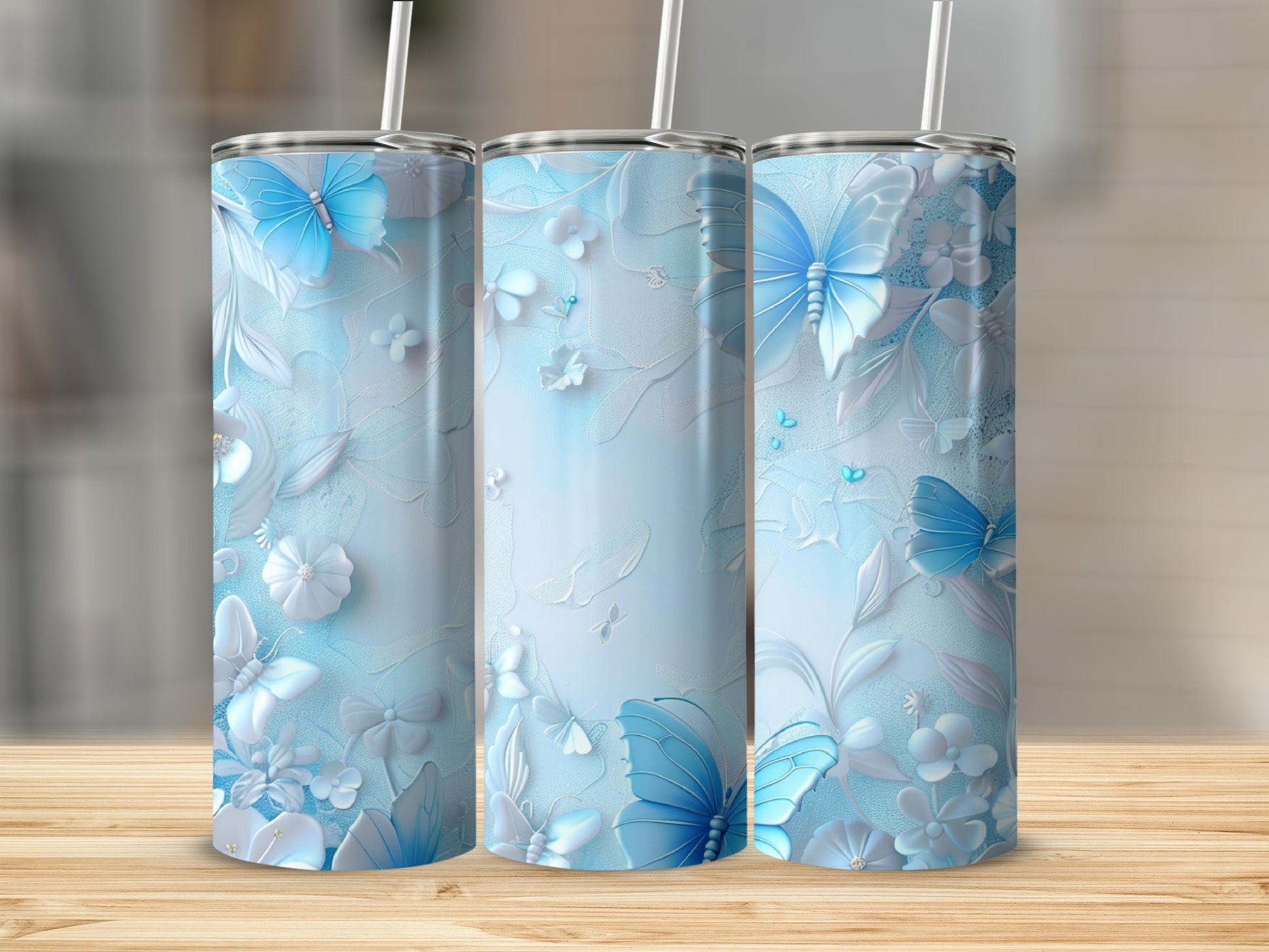 Three light blue tumblers with butterfly and floral relief patterns on a wooden surface.