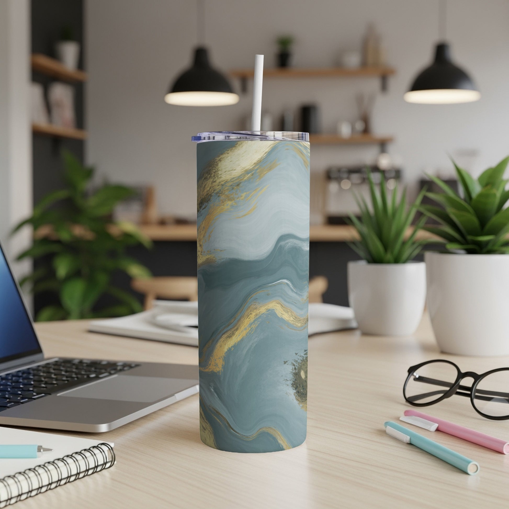 Blue and gold abstract pattern tumbler with straw on a desk.