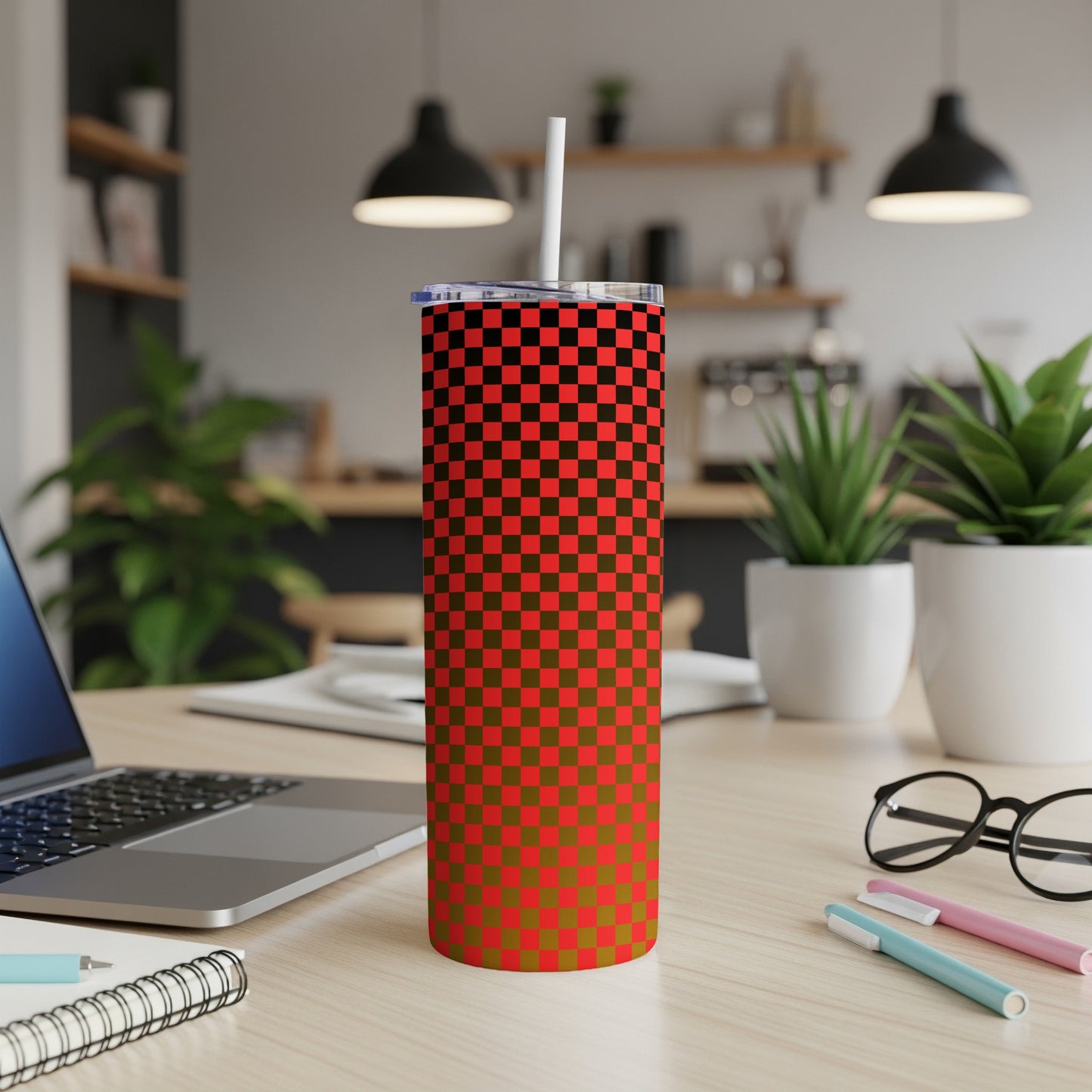 Checkerboard pattern tumbler with straw on a desk with laptop and plants.