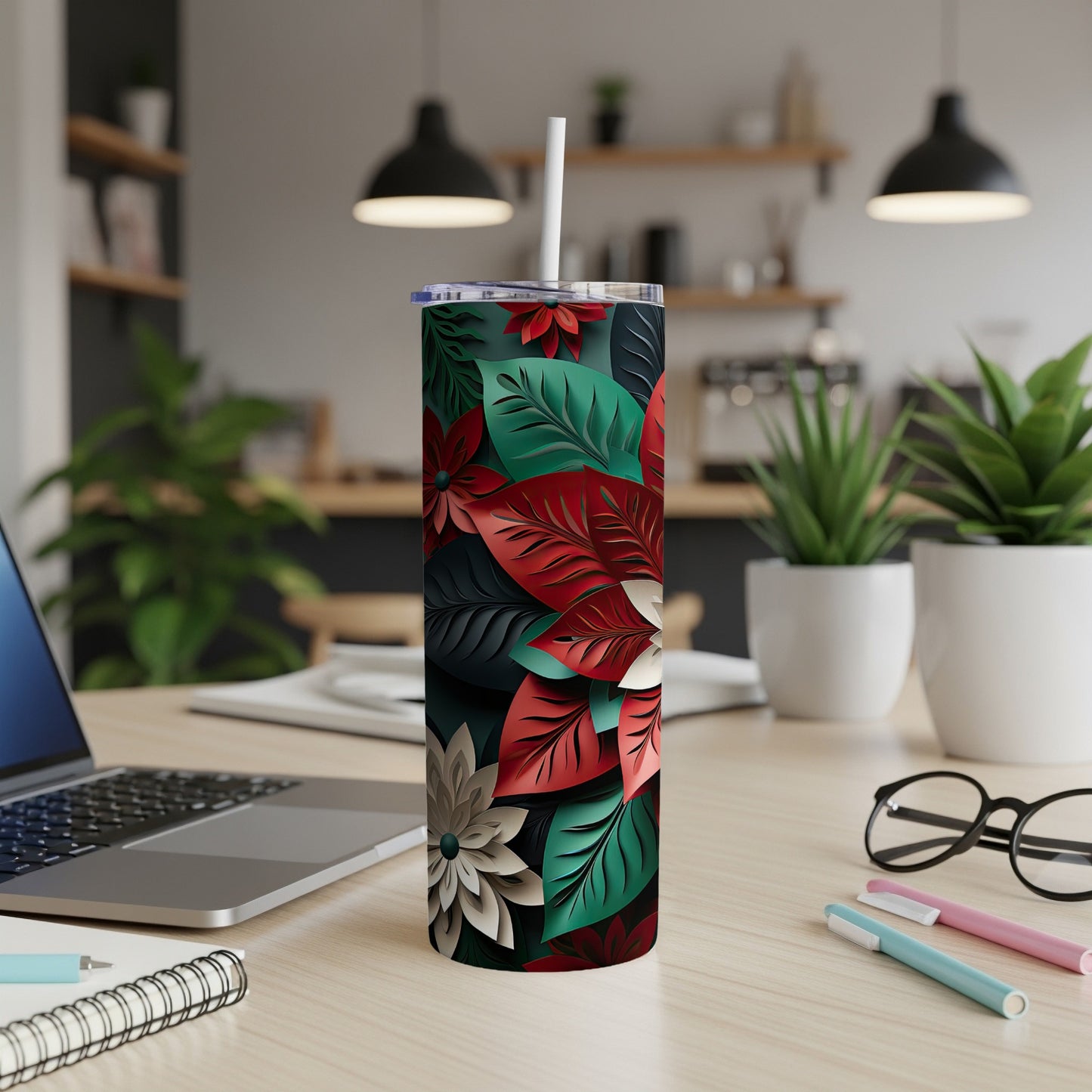Tall tumbler with poinsettia floral pattern, straw, on desk.