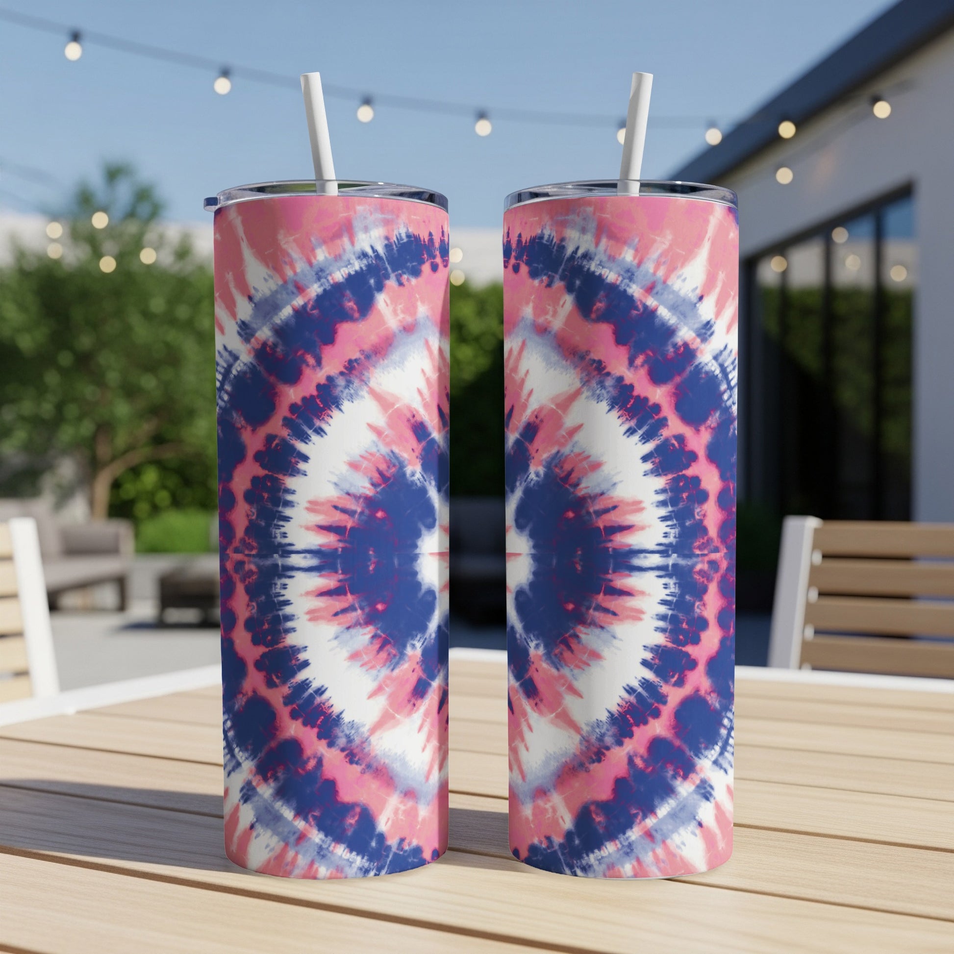 Two pink, blue, and white tie-dye tumblers with straws on a wooden table.