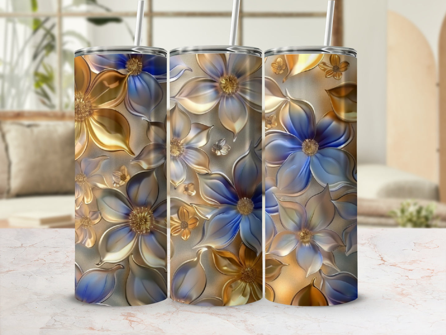 Three tumblers with golden and blue floral designs stand on a marble countertop.