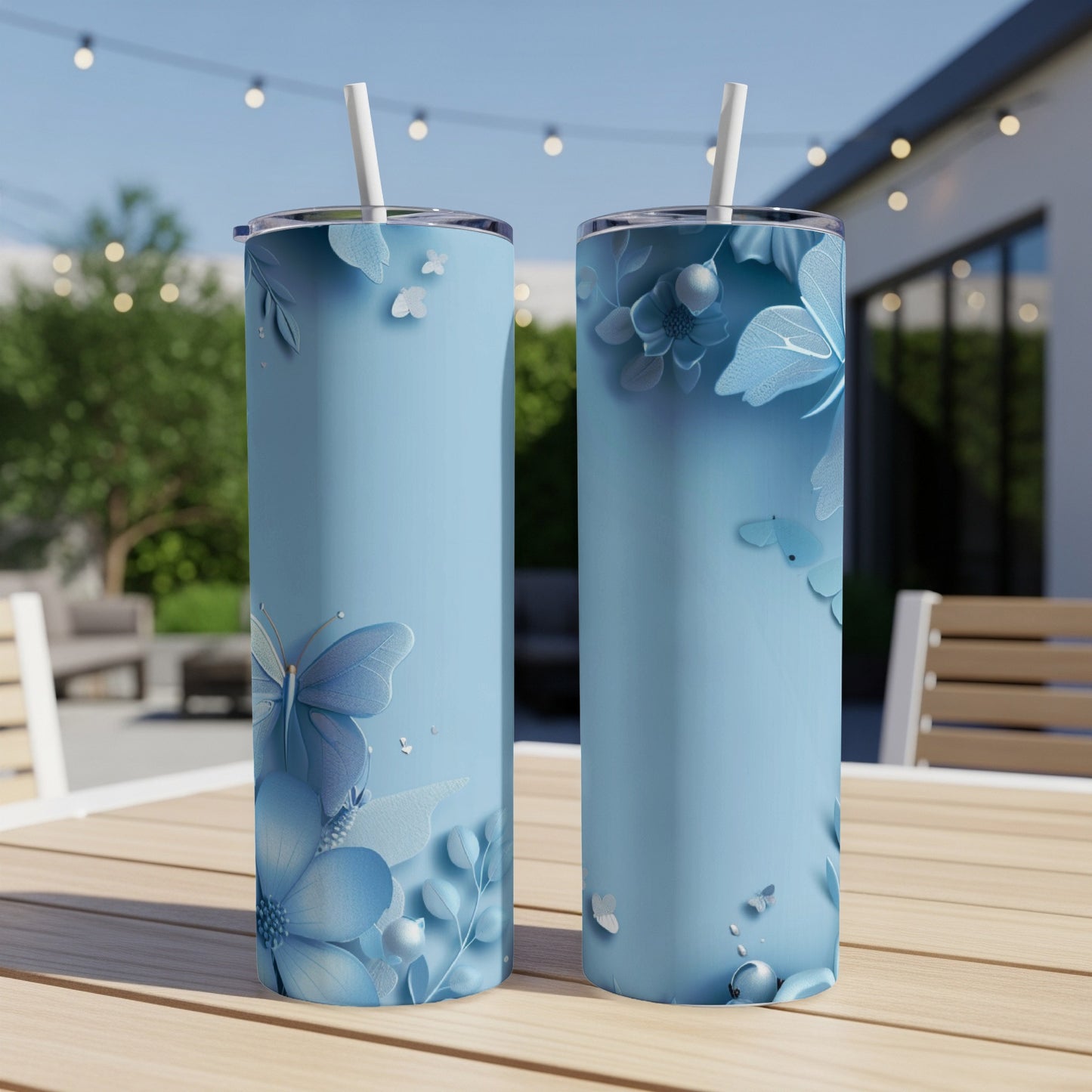 Two tall blue tumblers with butterfly and floral designs on an outdoor table.