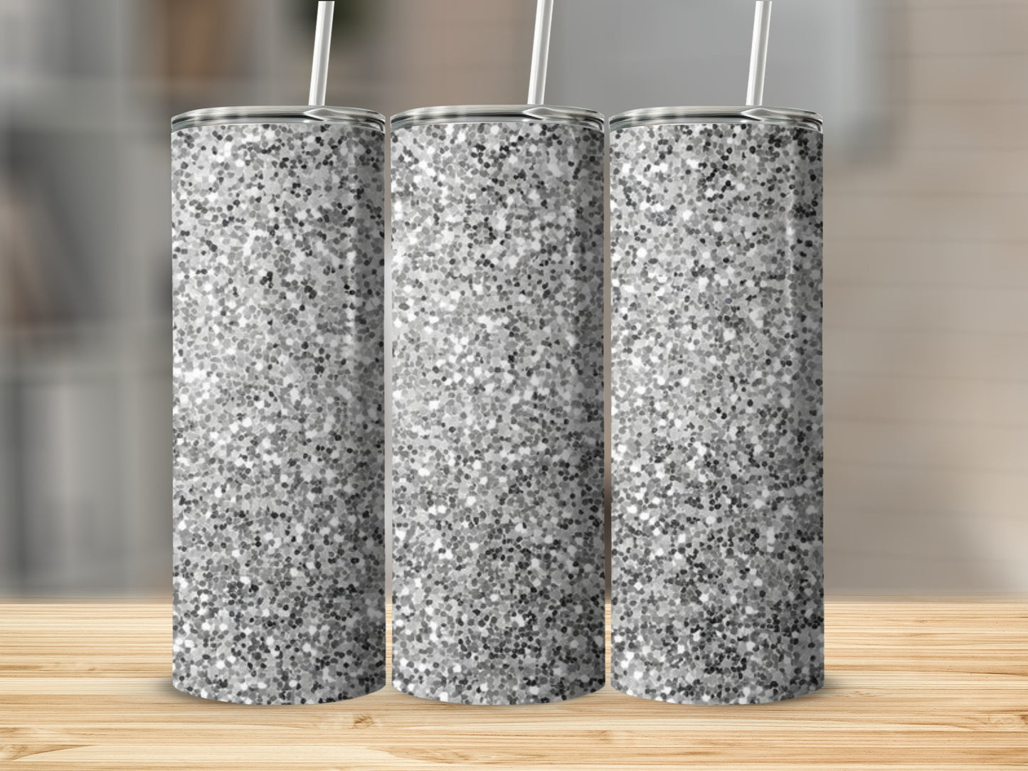 Three silver glitter tumblers with straws on a wooden surface.