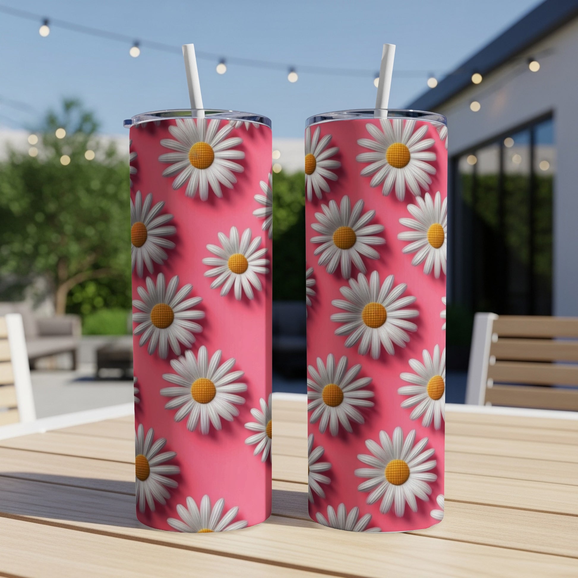 Two pink tumblers with white daisy pattern and straws sit on a table.