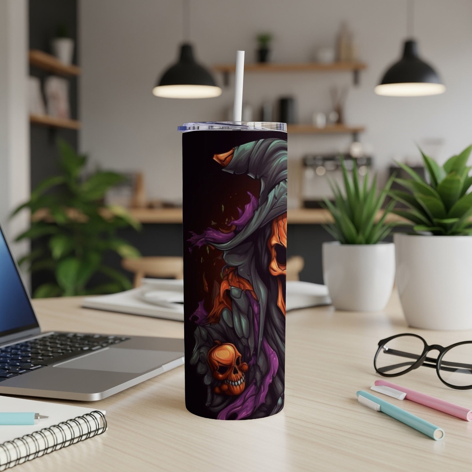 Halloween skull tumbler with a straw on a desk next to a laptop.