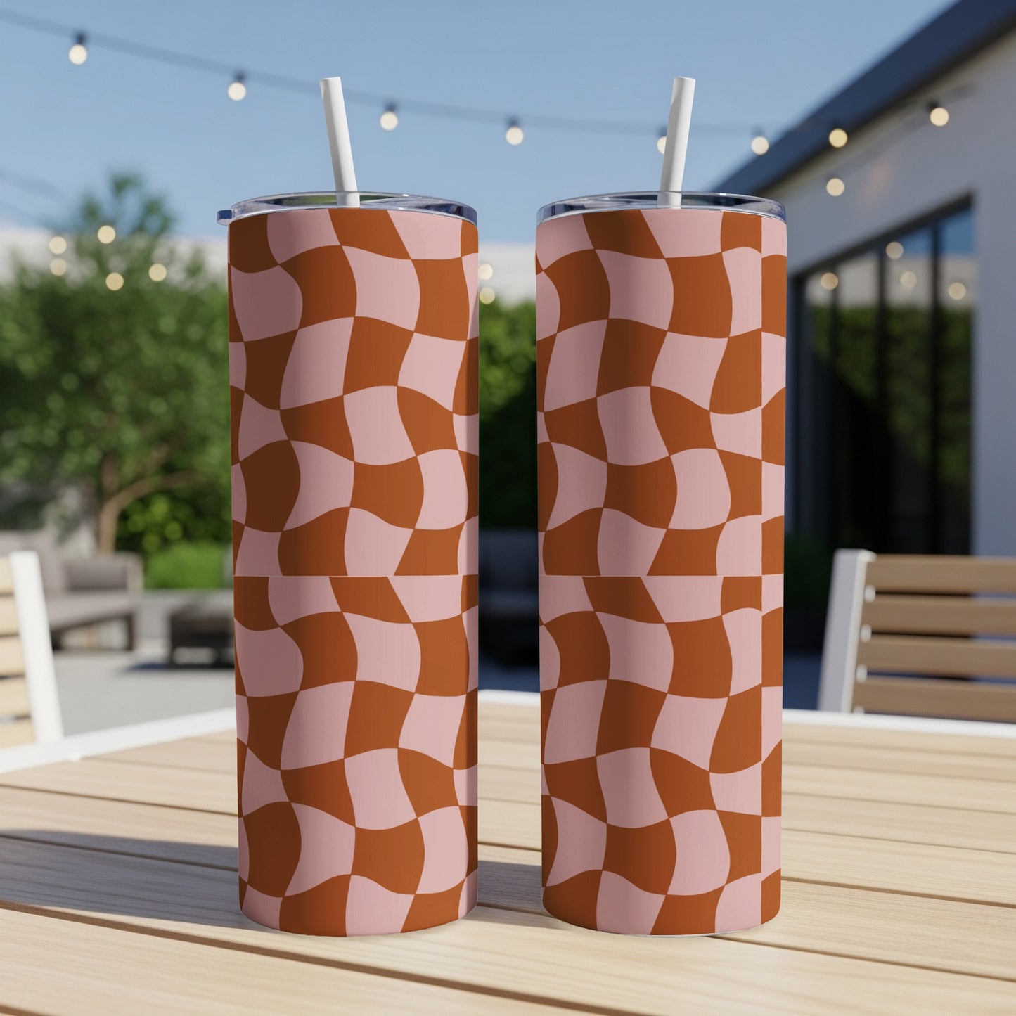 Two pink and brown checkered tumblers with straws on a wooden table.