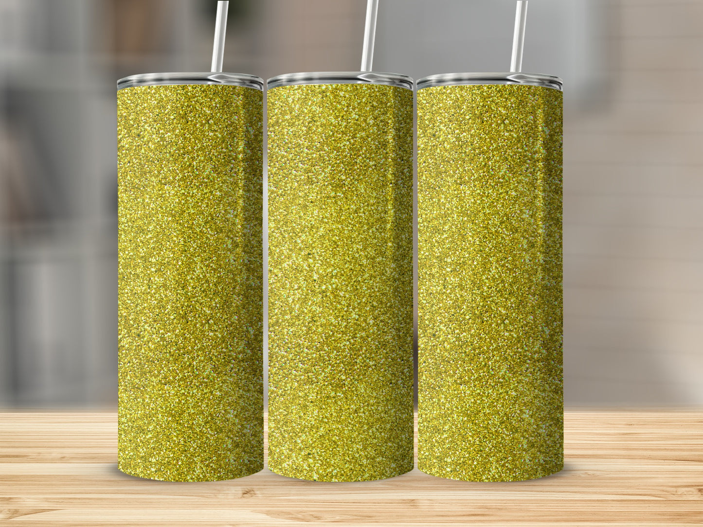 Three gold glitter tumblers with straws displayed on a wooden surface.