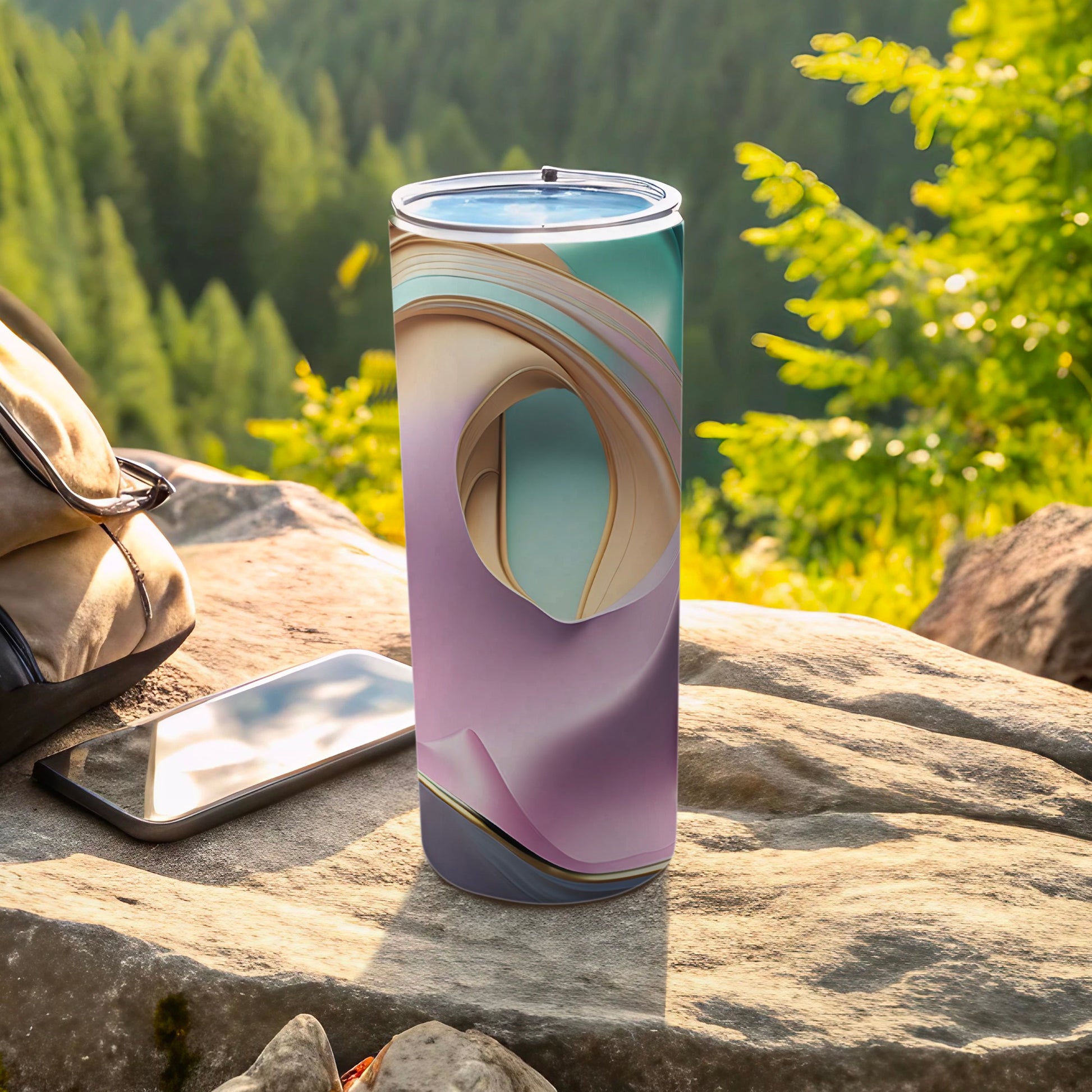 Tall tumbler with abstract pastel design sits on a rock, next to a phone and bag.