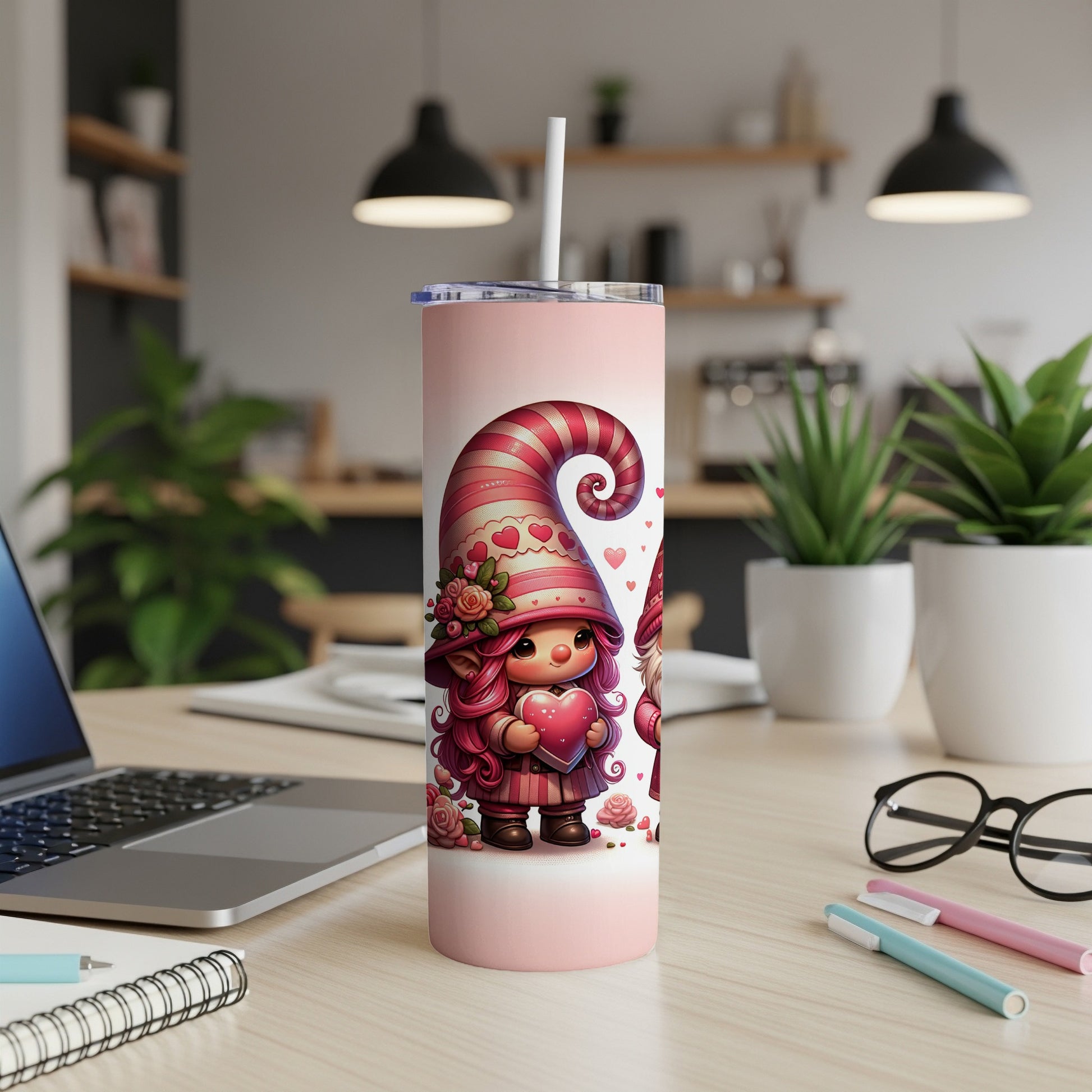 Pink gnome holding heart on a tumbler with a straw, laptop, and pens.