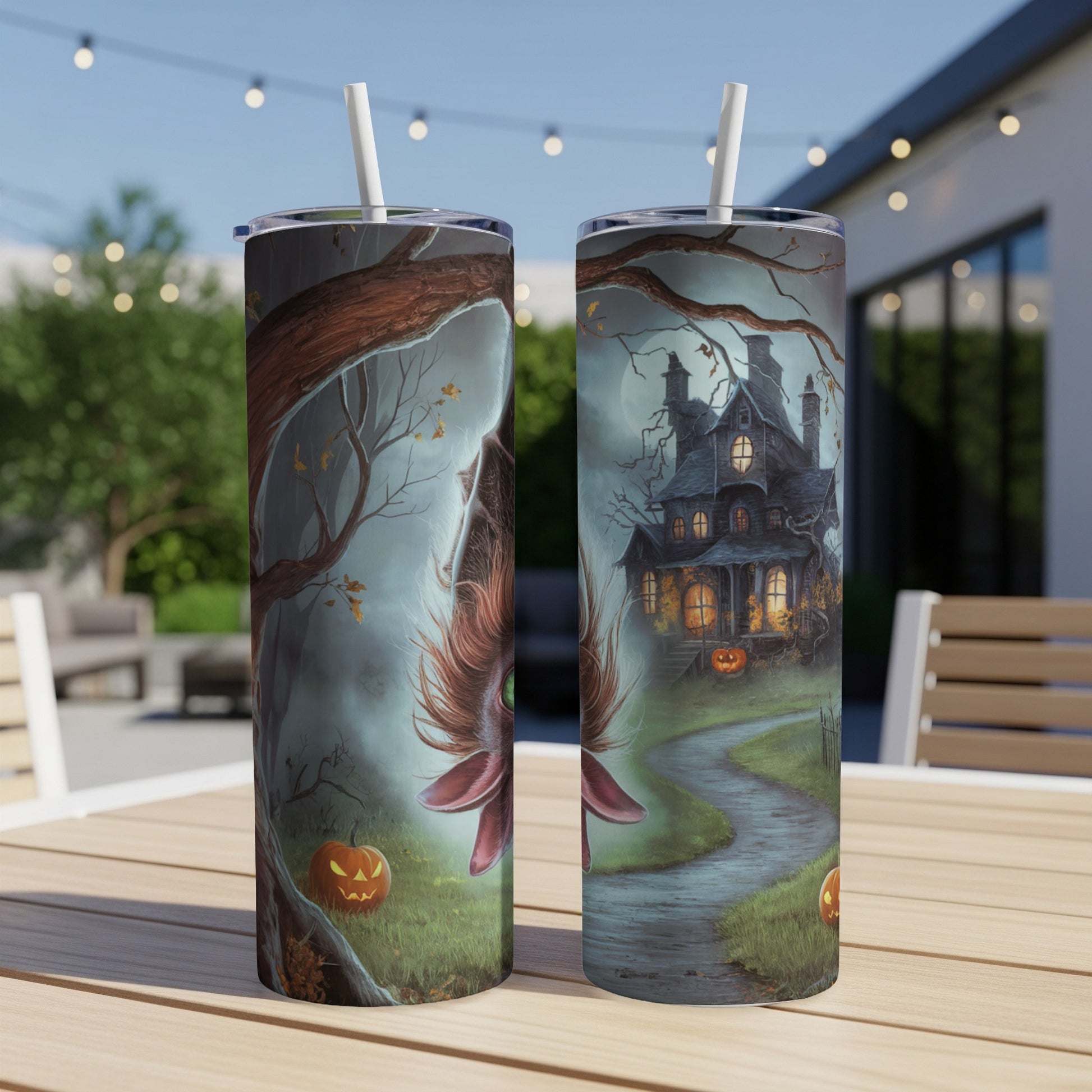 Two Halloween-themed tumblers, one with a bat, one with a haunted house, on a table.