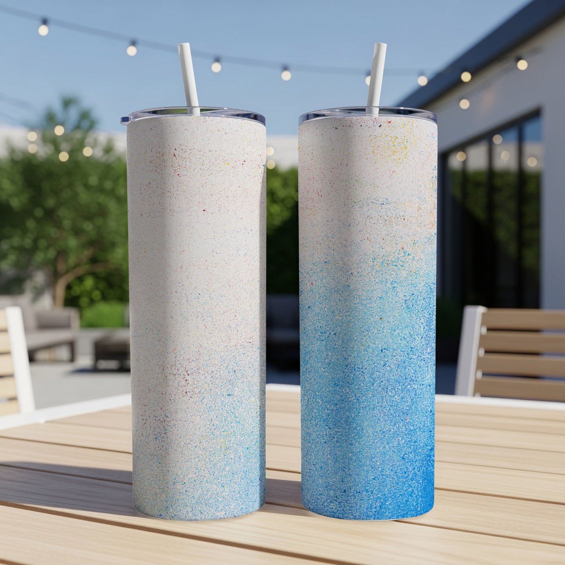 Two tall tumblers with colorful speckled designs and straws on a table.