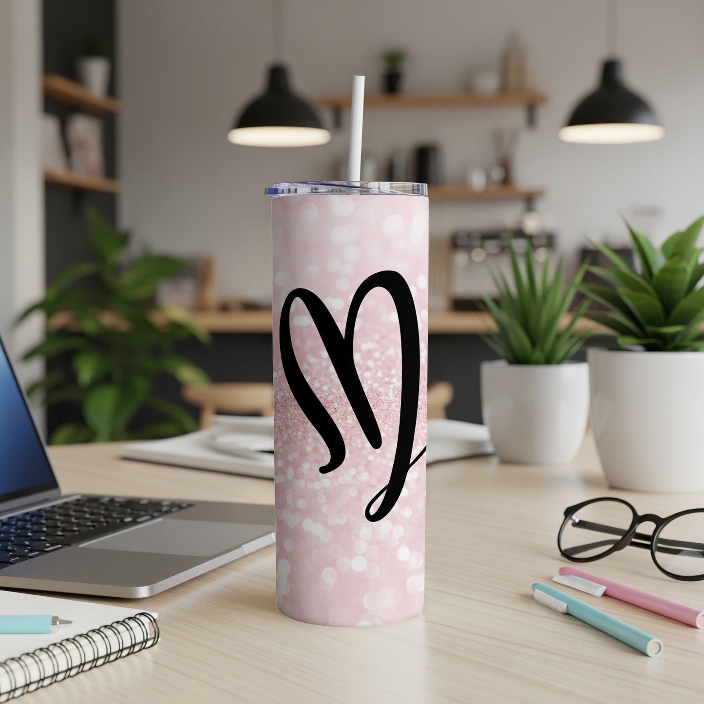 Pink glitter tumbler with black "MJ" monogram, on a desk.