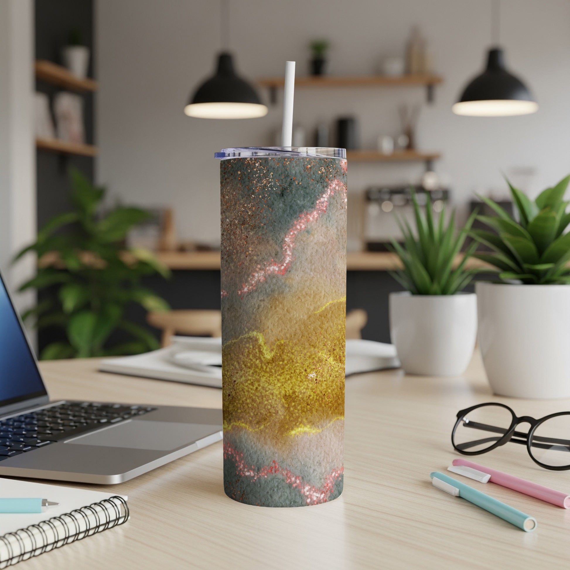 Glittery abstract pattern tumbler with straw on a desk with laptop.