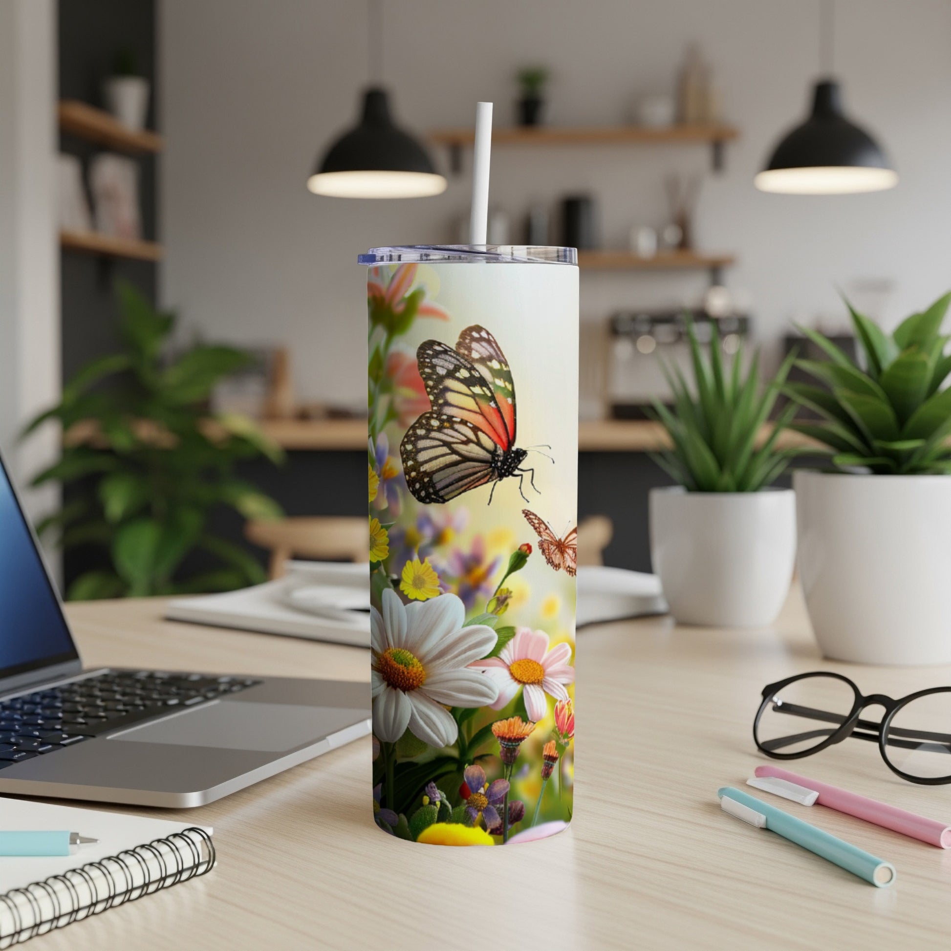 Floral tumbler with butterflies, daisies, and a straw on a desk.