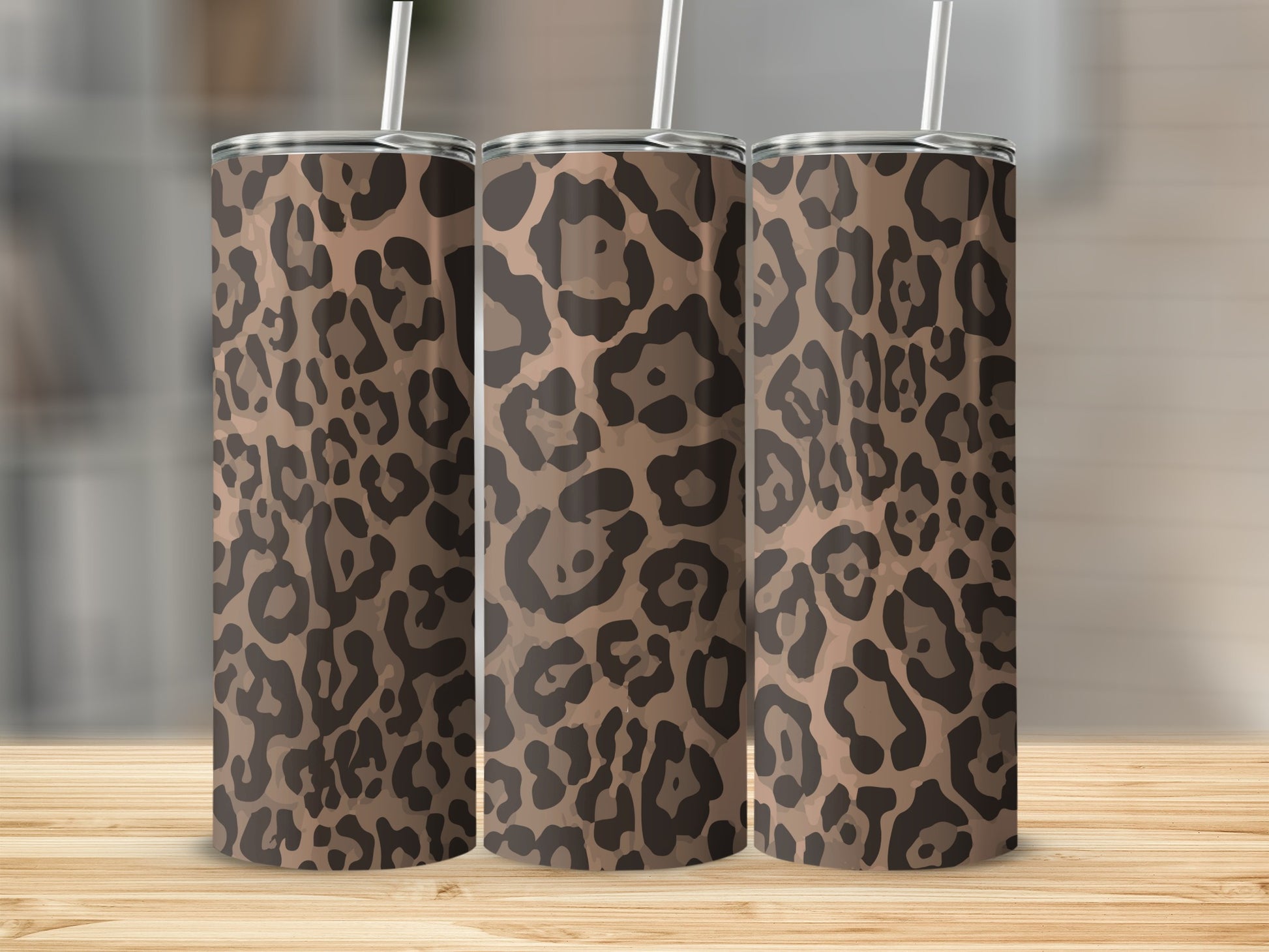 Three tumblers with leopard print design and straws on a wooden surface.