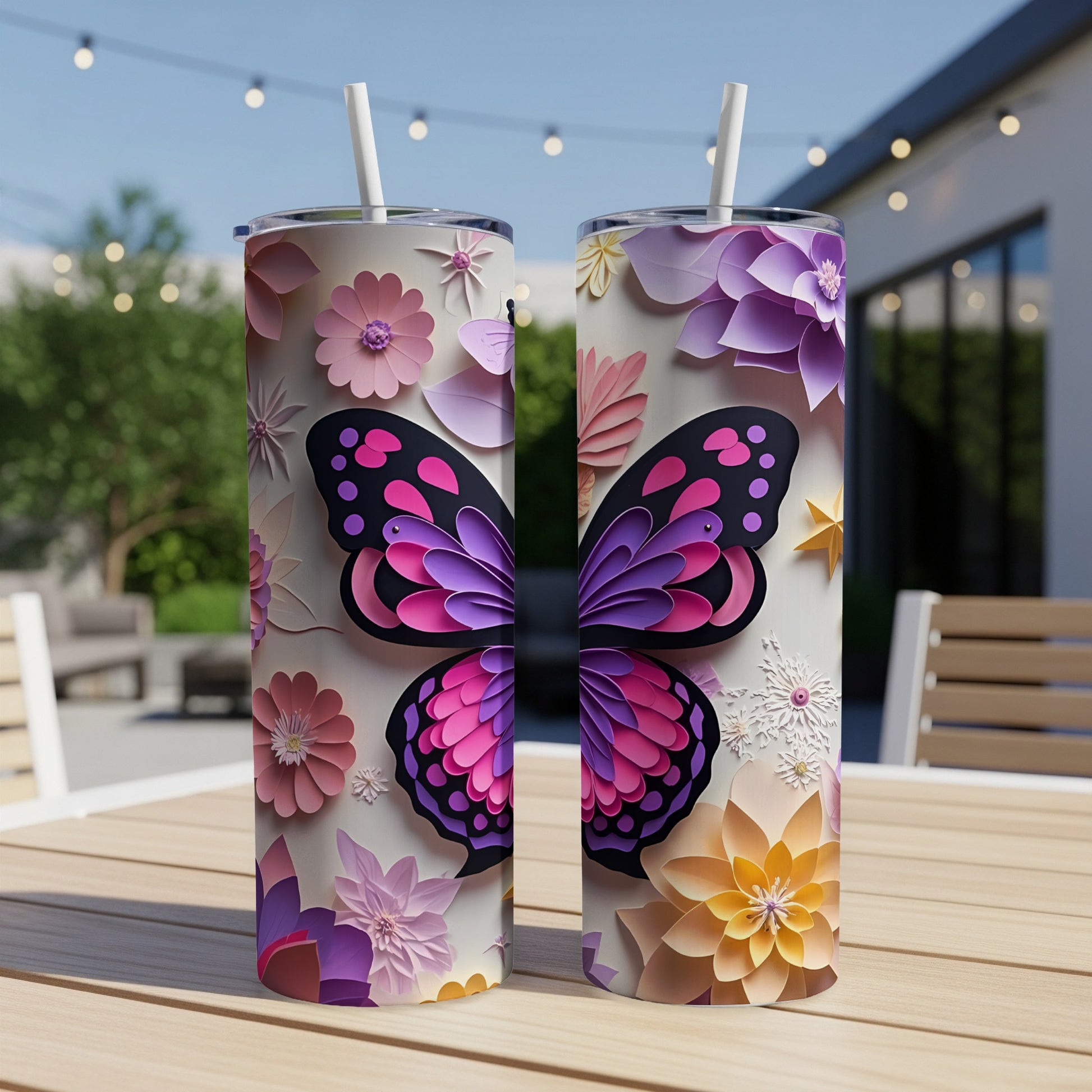 Two tumblers with colorful butterfly and floral designs sit on a wooden table outdoors.